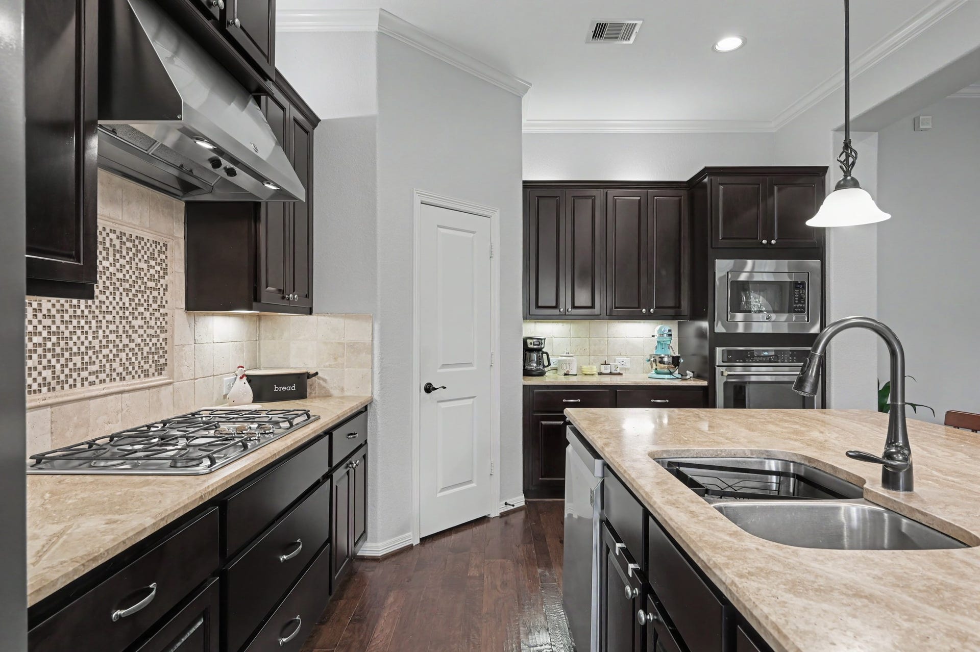 271 Rio Ranch Circle, Montgomery, TX 77316 Elegant kitchen with dark wood cabinetry, granite countertops, and a central island featuring a modern sink. Includes a gas cooktop, built-in ovens, and stylish tile backsplash.
