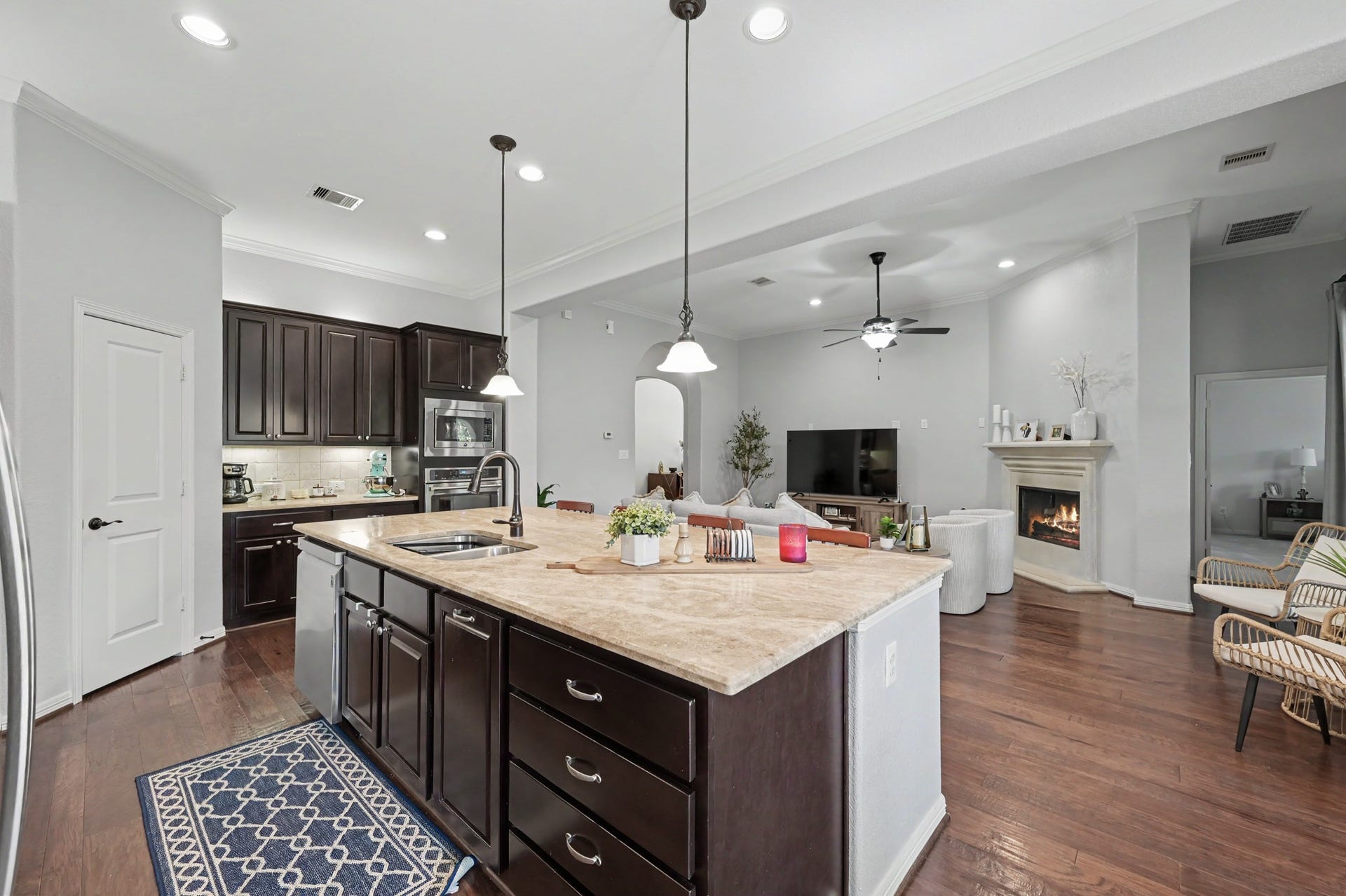 271 Rio Ranch Circle, Montgomery, TX 77316 Spacious open-concept living area featuring a modern kitchen with dark cabinetry, a large island, and pendant lighting, seamlessly flowing into a cozy living room with a fireplace and hardwood floors.