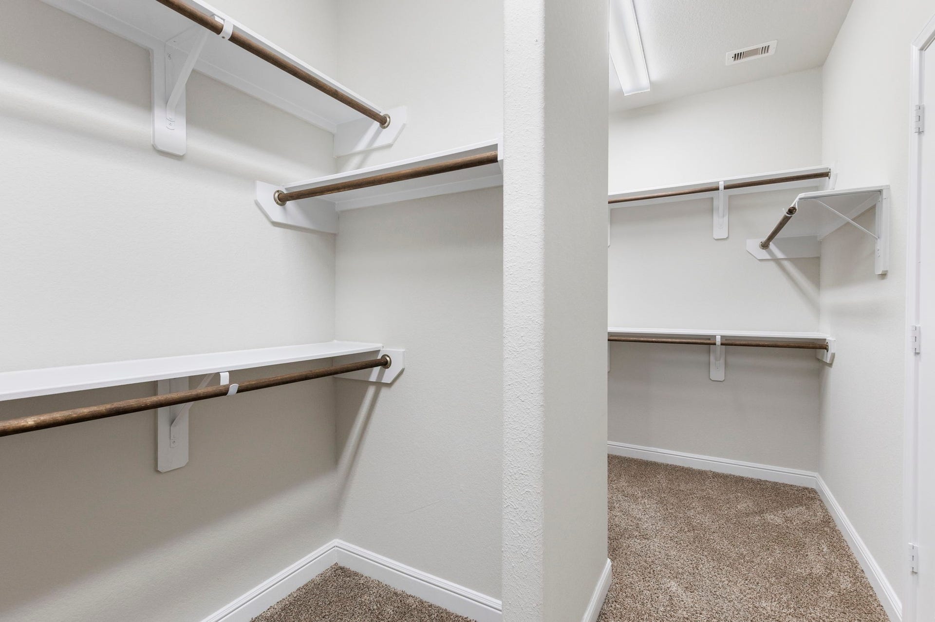 2819 Bradbury Hills Drive, Spring, TX 77373 This photo showcases a spacious walk-in closet with multiple wooden hanging rods and white shelving, offering ample storage space. The room is well-lit and has a neutral carpet flooring, creating a clean and organized atmosphere.