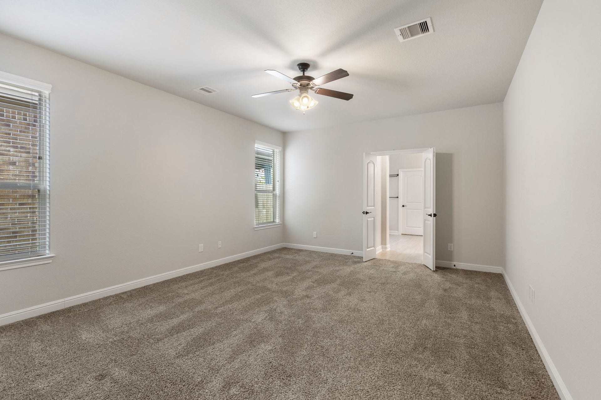 2819 Bradbury Hills Drive, Spring, TX 77373 This spacious primary bedroom offers a serene retreat with plush carpeting, abundant natural light from multiple windows, and elegant double doors leading to a luxurious ensuite.