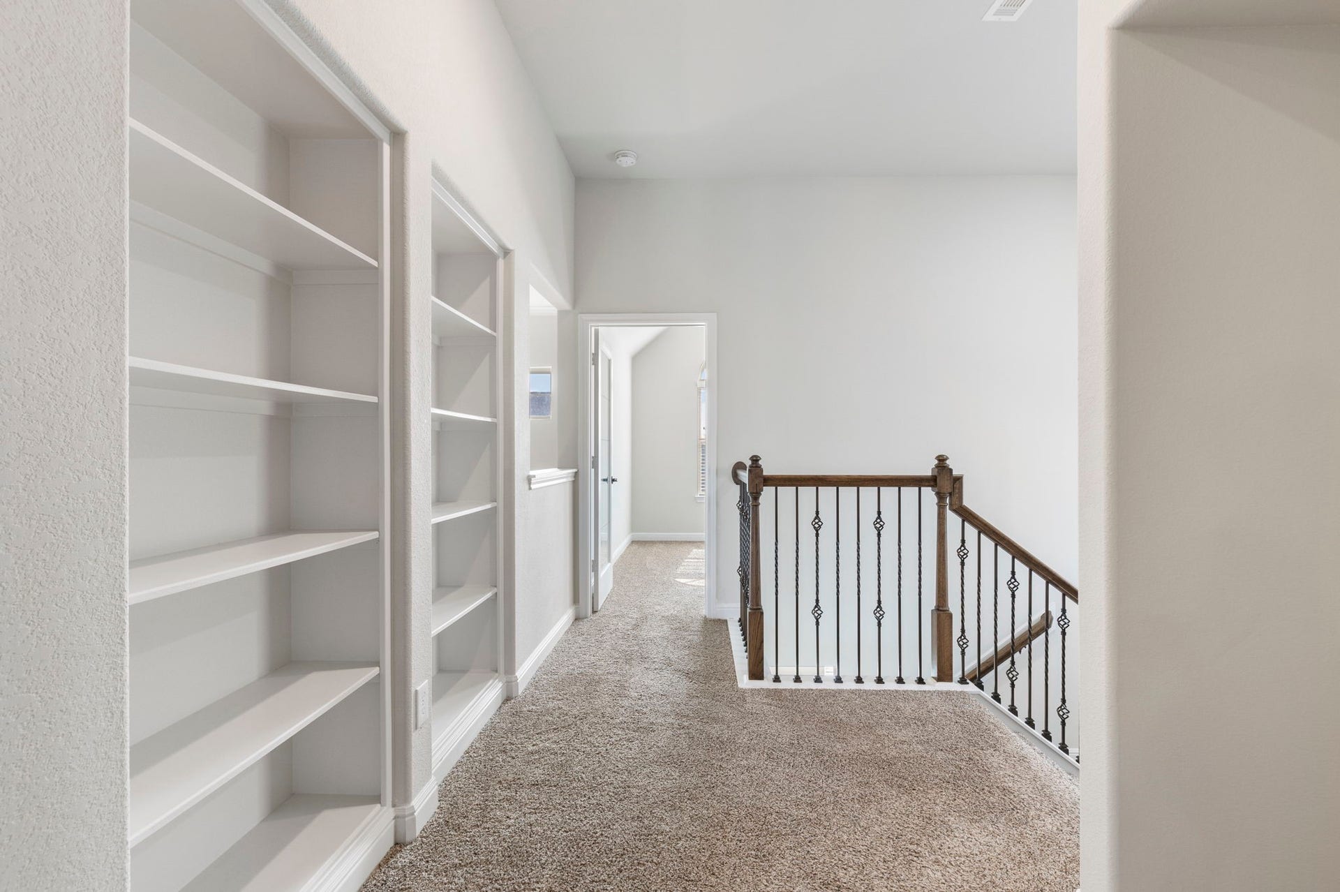 2819 Bradbury Hills Drive, Spring, TX 77373 This photo shows a bright hallway with built-in shelves and carpeted flooring. There's a staircase with a decorative railing leading downstairs, and a doorway to another room, creating a spacious and inviting upper-level space.