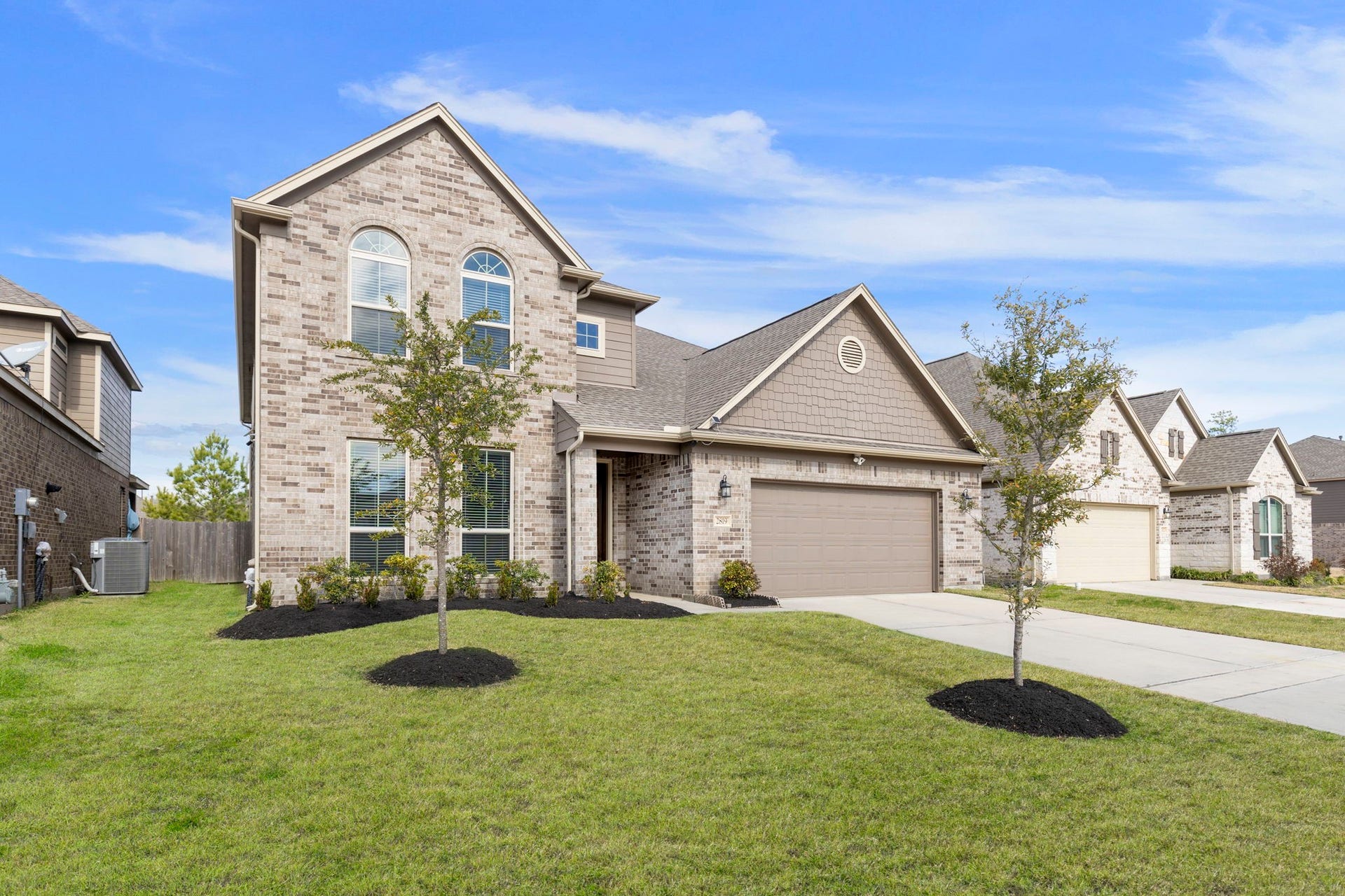 2819 Bradbury Hills Drive, Spring, TX 77373 This photo showcases a modern two-story brick home with a well-maintained lawn and young trees. It features a two-car garage, a gabled roof, and large arched windows, offering a blend of elegance and functionality in a suburban neighborhood.