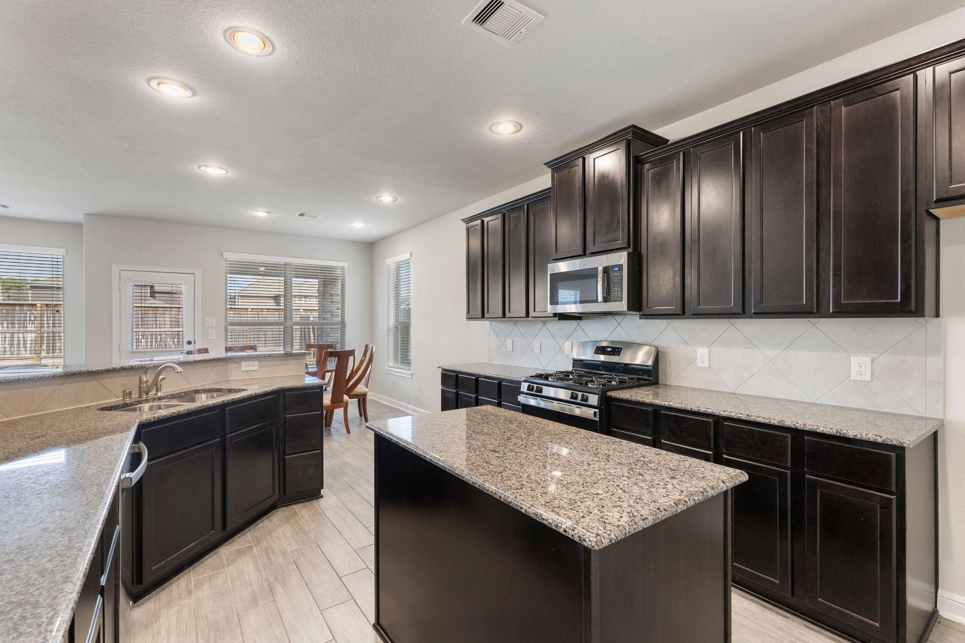 2819 Bradbury Hills Drive, Spring, TX 77373 This modern kitchen features dark wood cabinets, granite countertops, and stainless steel appliances. It's spacious with an island, recessed lighting, and plenty of natural light from large windows. Perfect for cooking and entertaining.