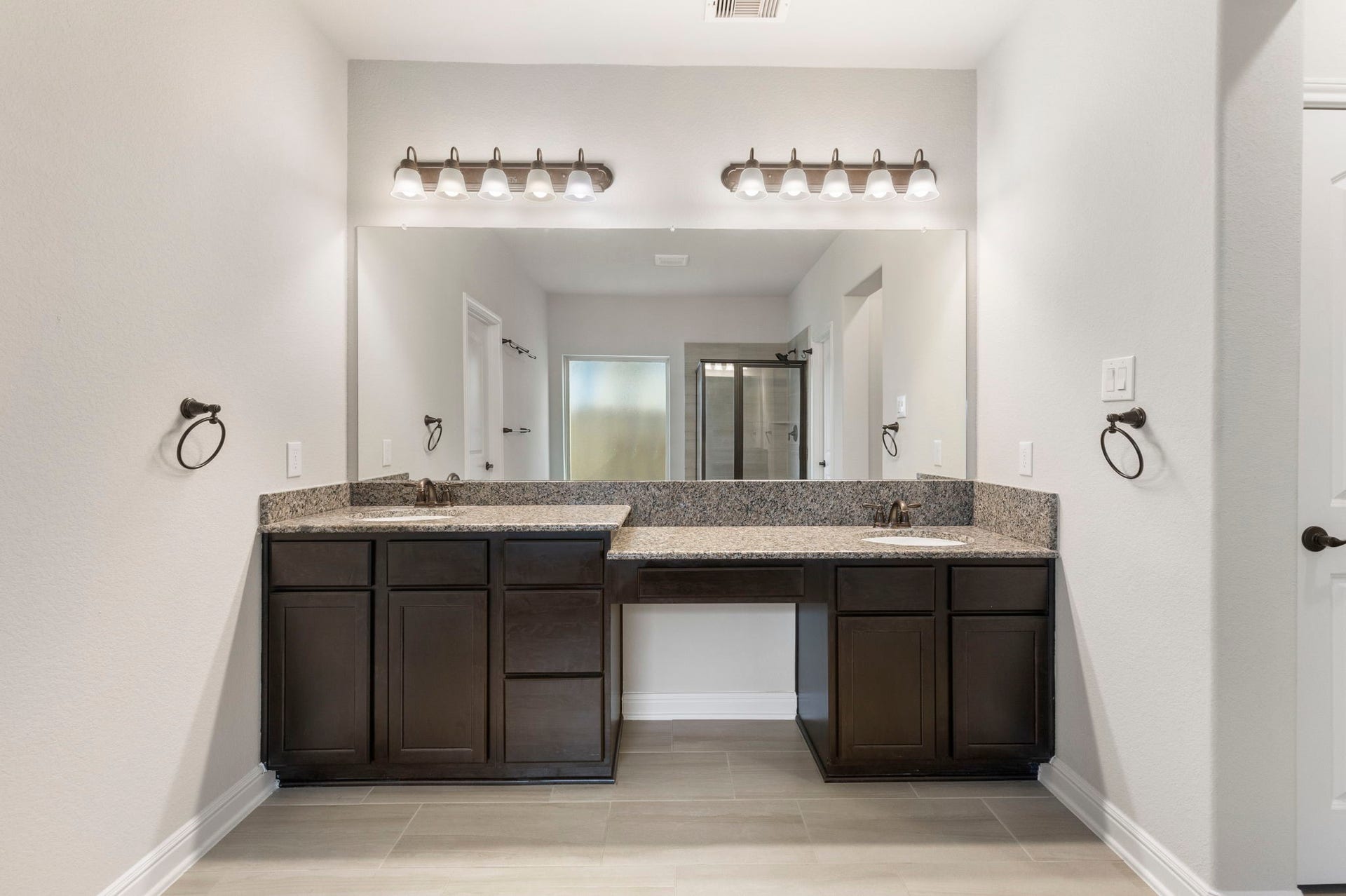 2819 Bradbury Hills Drive, Spring, TX 77373 This photo features a modern bathroom with dual sinks and dark wood cabinetry, granite countertops, and a large mirror with overhead lighting. The space is bright with neutral wall colors and tile flooring.