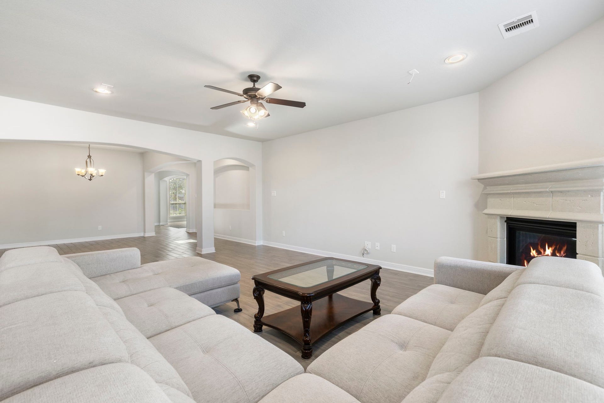 2819 Bradbury Hills Drive, Spring, TX 77373 This spacious living area features an elegant fireplace, cozy sectional sofa, and a ceiling fan. It has an open layout with archways leading to additional spaces, complemented by wood flooring and neutral walls for a modern, inviting atmosphere.
