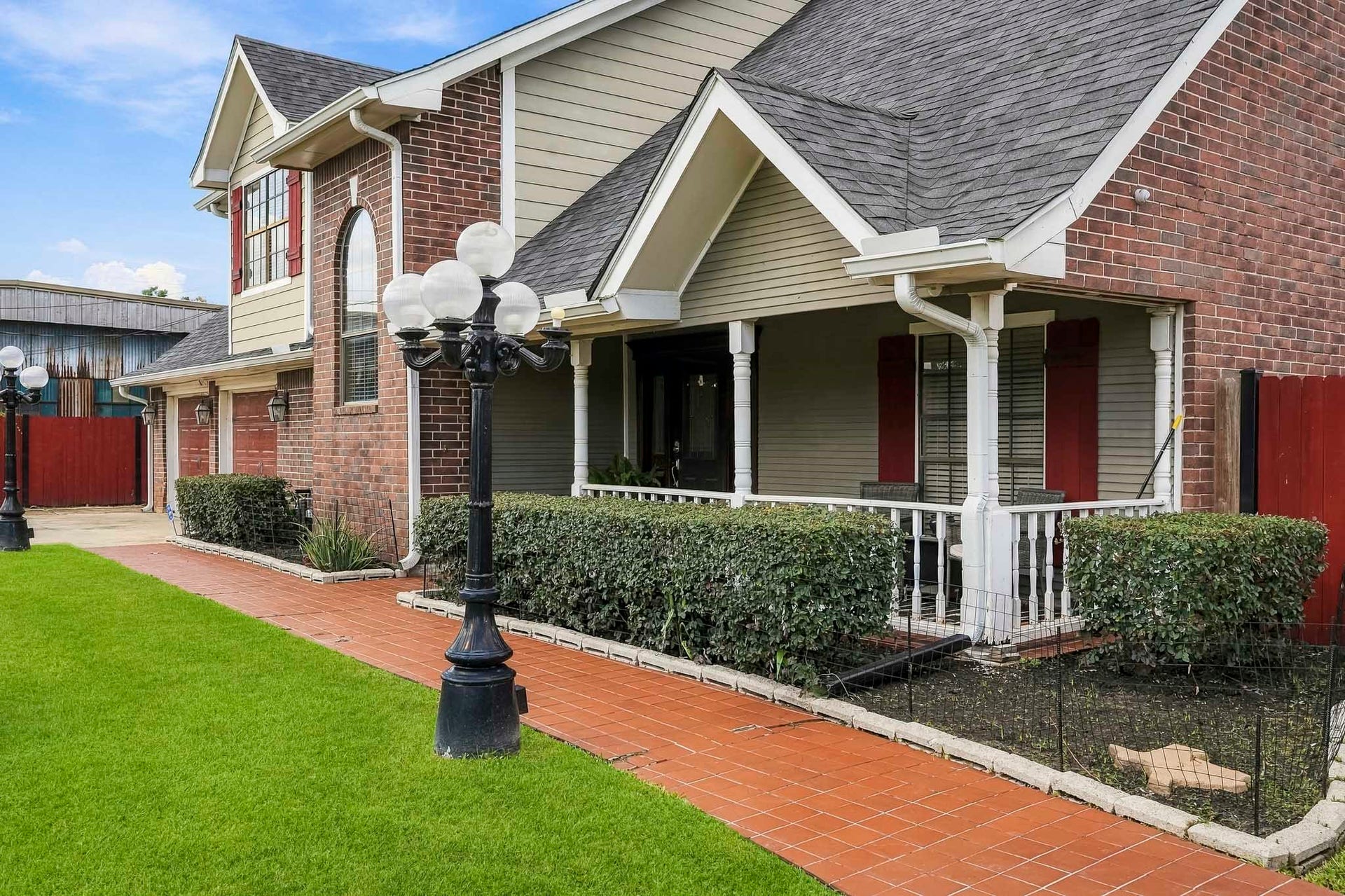 1207 9th Street, Galena Park, TX 77547 Charming two-story home with a classic brick facade, inviting front porch, and manicured landscaping, featuring elegant lamp posts lining the walkway.
