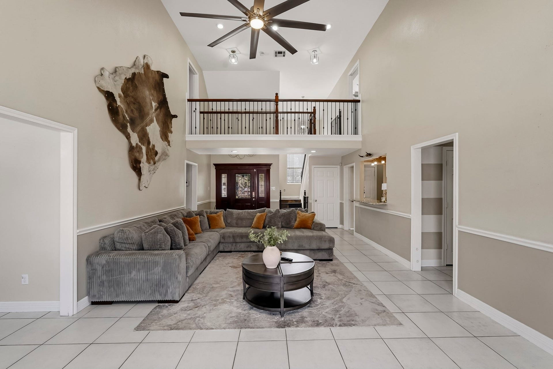 1207 9th Street, Galena Park, TX 77547 Spacious living area with high ceilings and a modern fan, featuring a cozy sectional sofa and stylish decor. A second-floor balcony overlooks the room, adding to the open, airy feel.