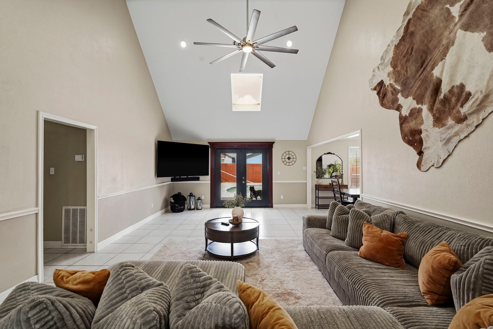 1207 9th Street, Galena Park, TX 77547 Spacious living room with vaulted ceilings, a modern ceiling fan, and natural light from a skylight. Sliding glass doors lead to an outdoor space that features a beautiful pool, enhancing indoor-outdoor living.