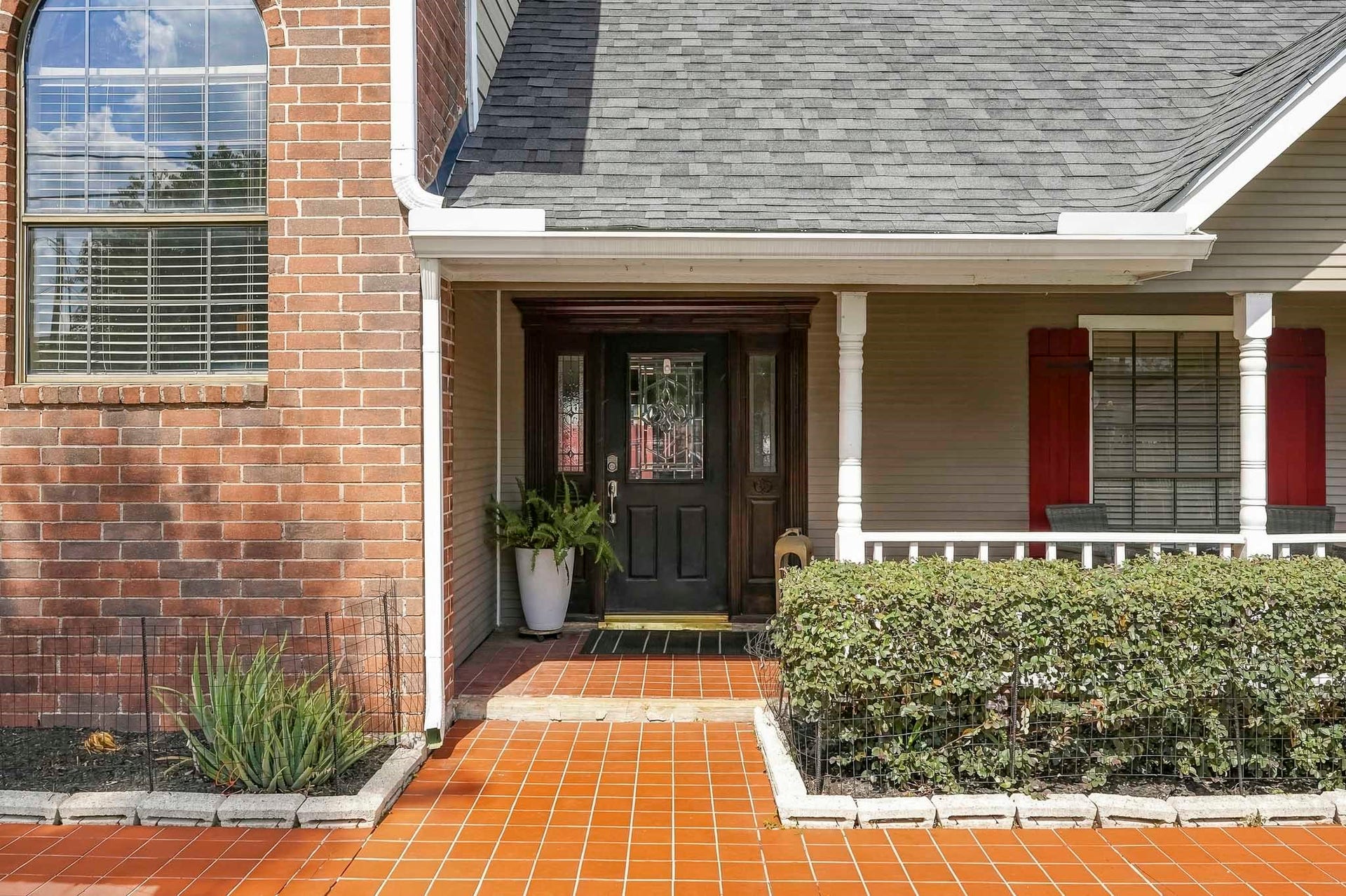 1207 9th Street, Galena Park, TX 77547 Charming entryway with a welcoming front porch, elegant black door, and vibrant red shutters, complemented by a lush hedge and tasteful brickwork.