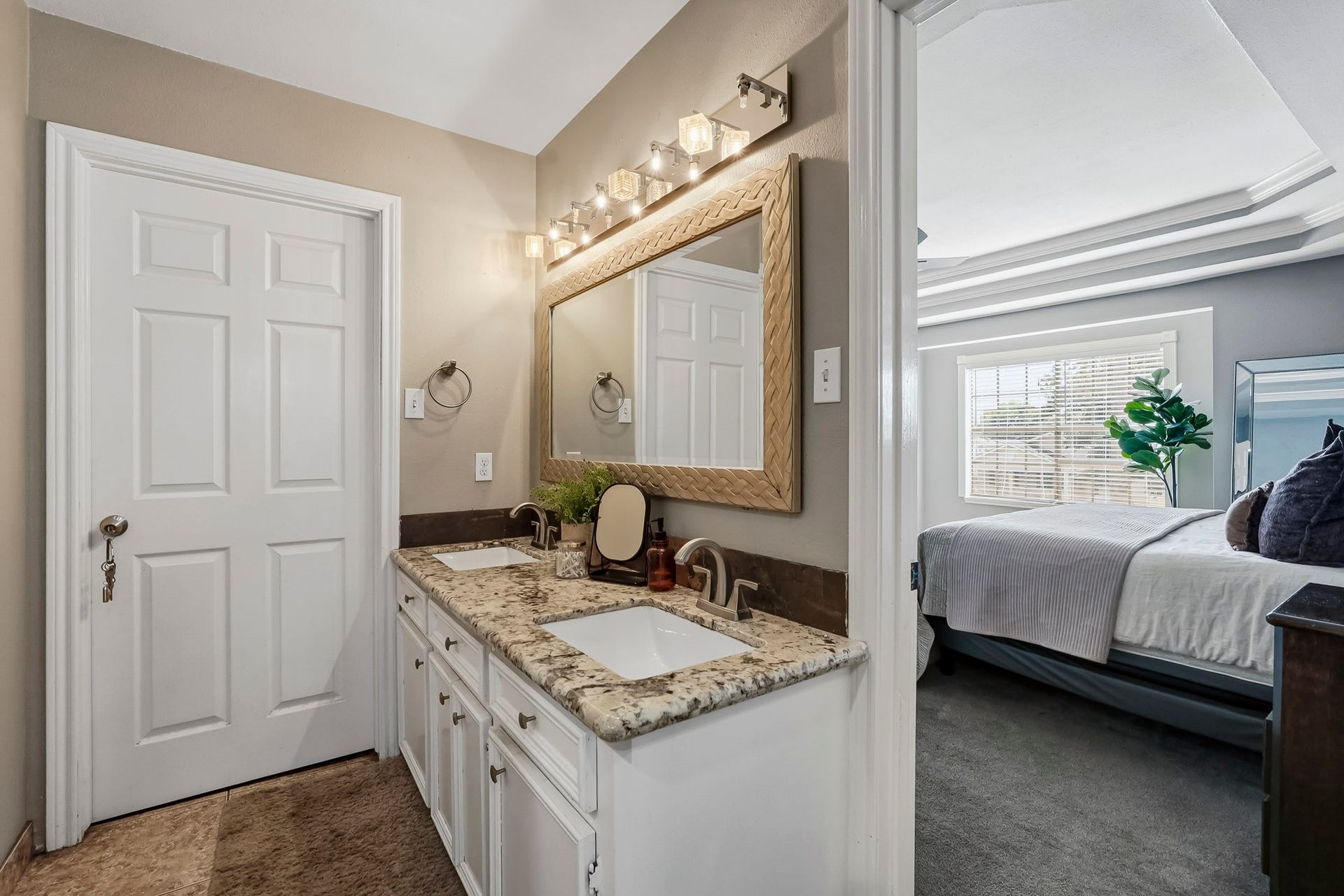 1207 9th Street, Galena Park, TX 77547 Elegant primary bathroom with a dual-sink vanity, granite countertops, and a large mirror, adjacent to a cozy, well-lit bedroom.