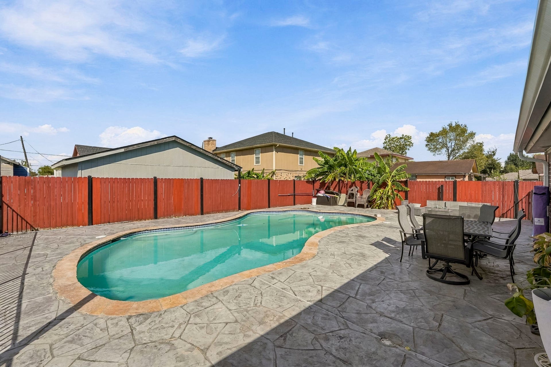 1207 9th Street, Galena Park, TX 77547 Enjoy sunny days in this spacious backyard featuring a sparkling pool, surrounded by a stylish stamped concrete patio and a vibrant red fence for privacy. Perfect for outdoor dining and relaxation.