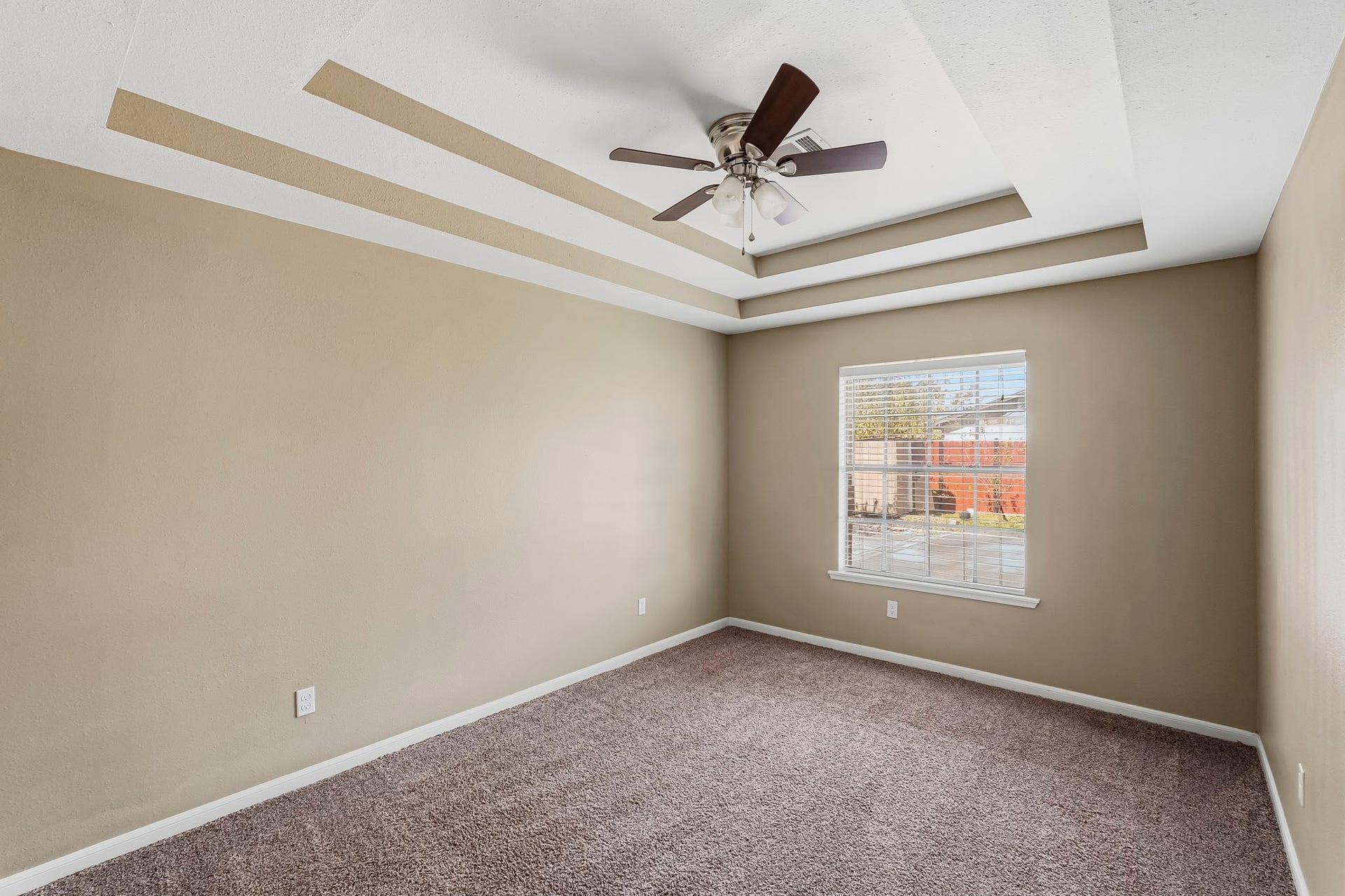 1207 9th Street, Galena Park, TX 77547 Spacious secondary bedroom with a stylish tray ceiling, ceiling fan, and soft carpeting, offering ample natural light through a large window.