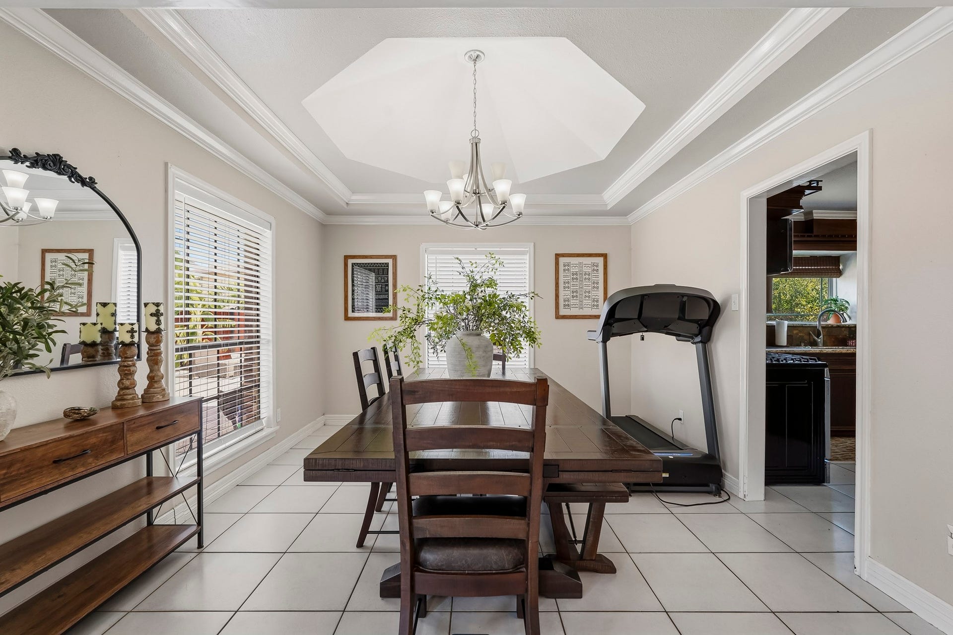 1207 9th Street, Galena Park, TX 77547 Bright dining room with elegant tray ceiling, modern chandelier, and large windows allowing natural light. Features a spacious wooden table, decorative shelving, and convenient access to the kitchen.
