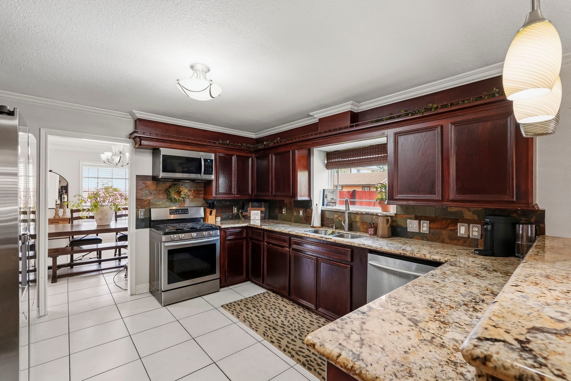 1207 9th Street, Galena Park, TX 77547 Elegant kitchen with rich dark wood cabinetry, granite countertops, and modern stainless steel appliances, seamlessly flowing into a bright dining area.