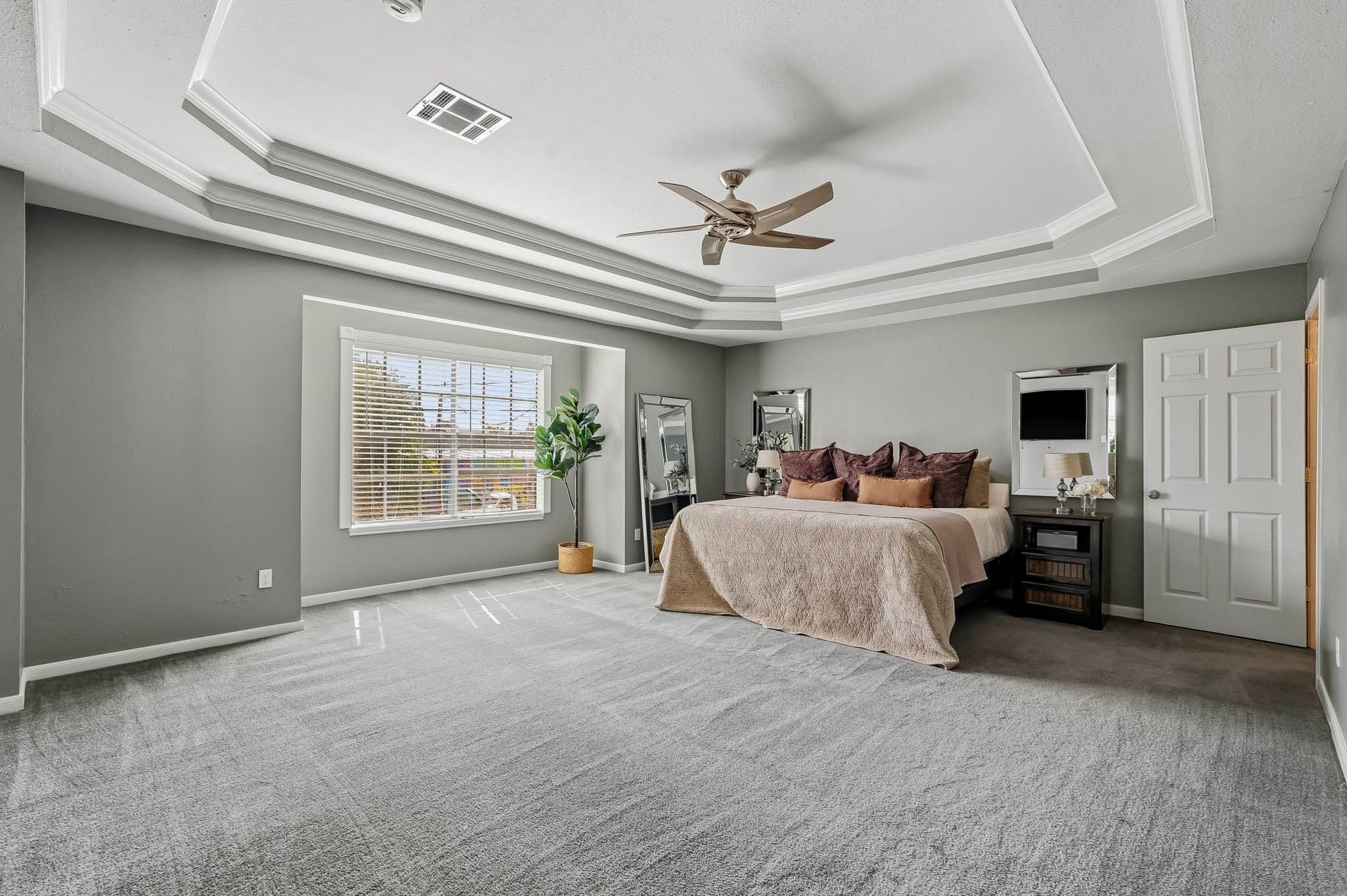 1207 9th Street, Galena Park, TX 77547 Spacious primary bedroom featuring elegant tray ceilings, a ceiling fan, and abundant natural light from a large window, creating a serene retreat.