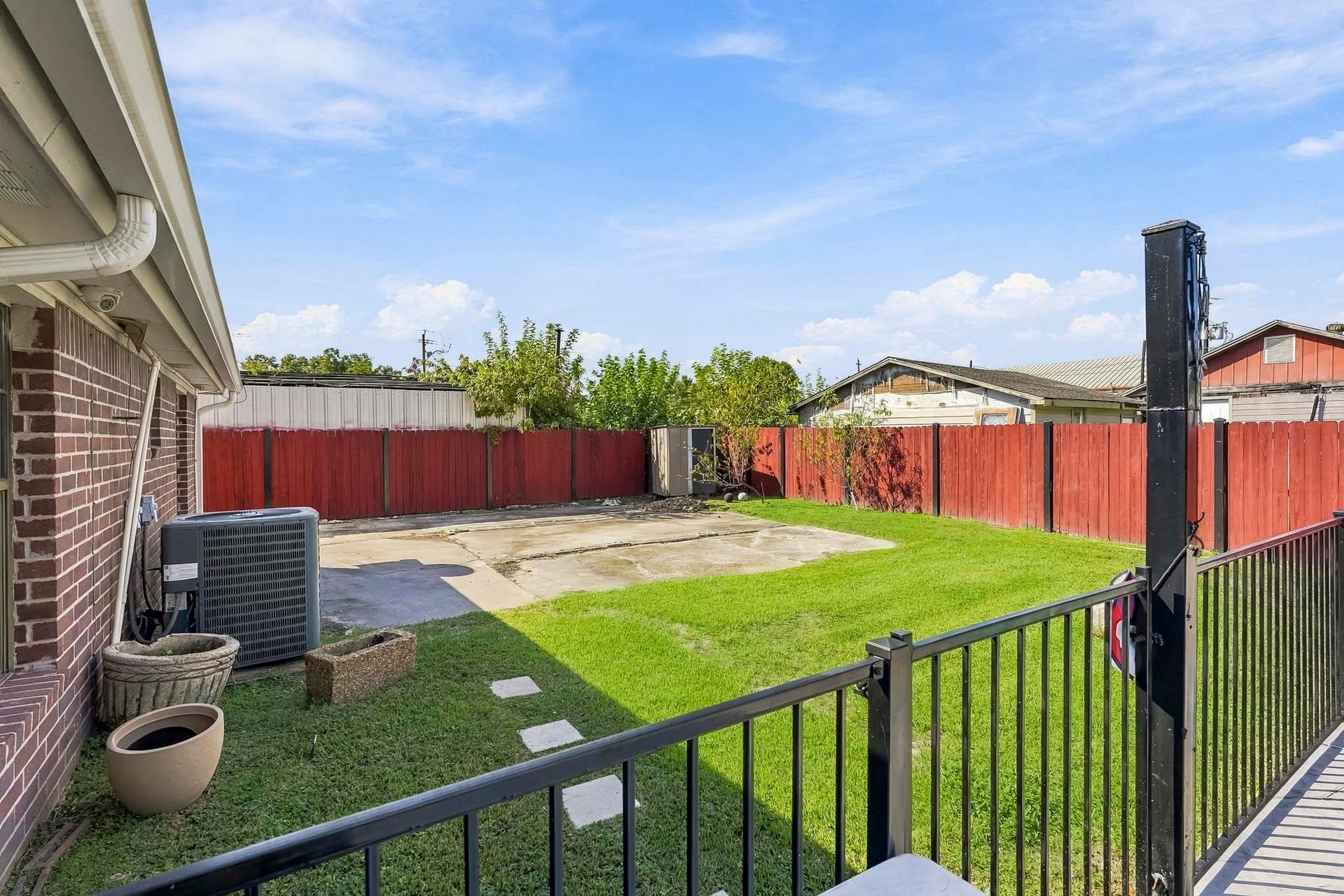 1207 9th Street, Galena Park, TX 77547 Charming backyard with a spacious lawn, red wooden fence, and patio area, perfect for outdoor entertaining and relaxation.