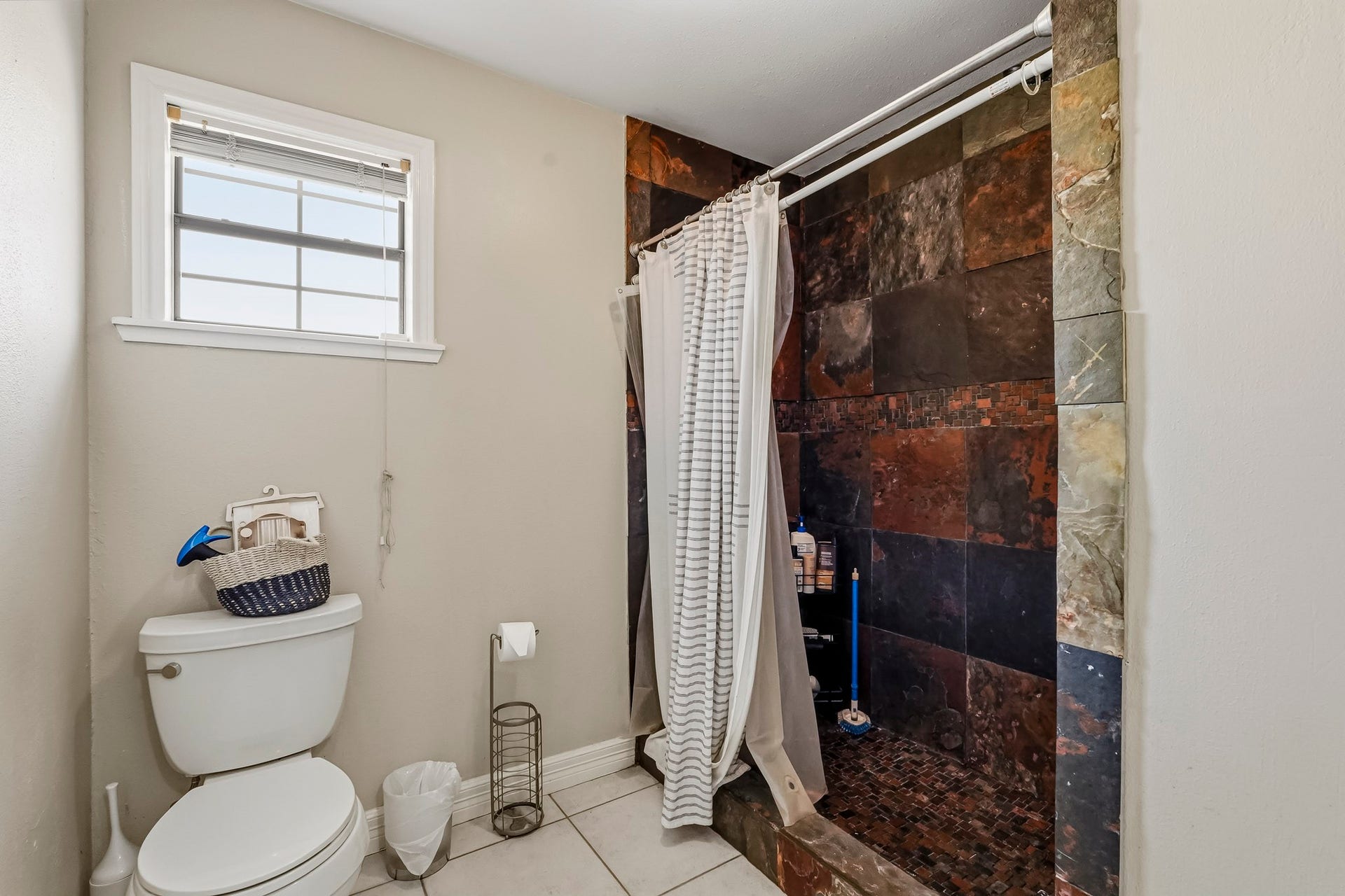 1207 9th Street, Galena Park, TX 77547 Modern secondary bathroom featuring a spacious walk-in shower with striking dark tile accents, complemented by a convenient toilet and a window for natural light.