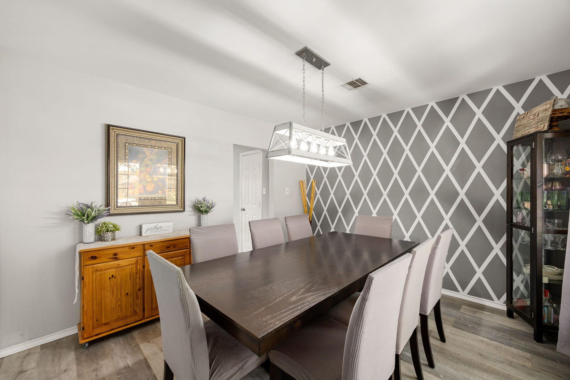 3915 Eastland Lake Drive, Richmond, TX 77406 The formal dining room features engineered wood flooring, a geometric accent wall design, and a modern light fixture.