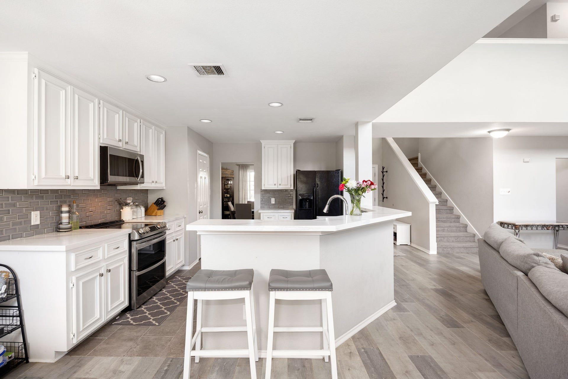 3915 Eastland Lake Drive, Richmond, TX 77406 This gourmet kitchen acts as a functional center with a raised breakfast bar, double ovens, white cabinetry, and a dark tile backsplash.