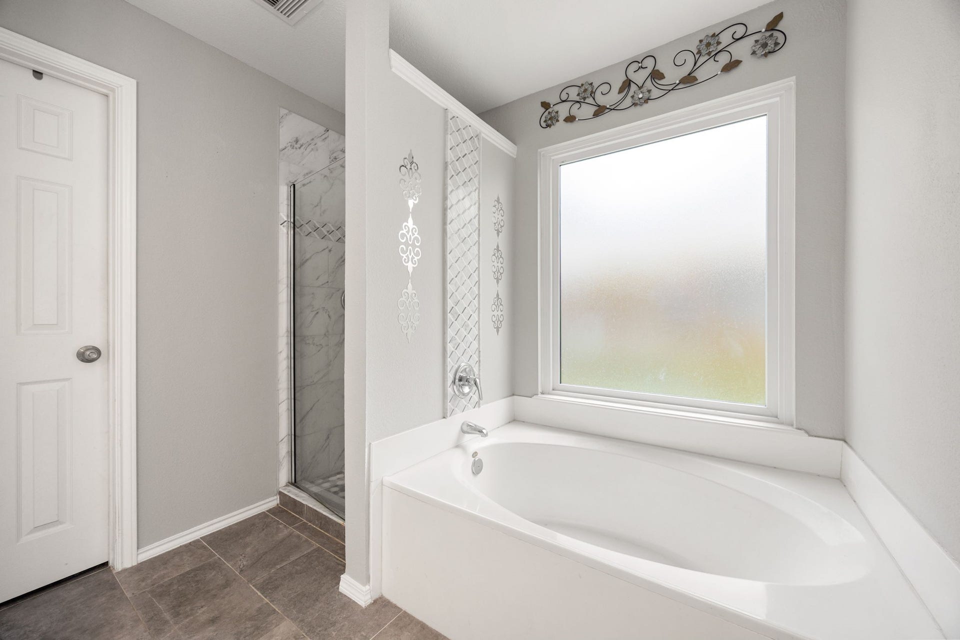 3915 Eastland Lake Drive, Richmond, TX 77406 Serving the primary suite, this refined relaxation space features an oval soaking tub positioned beneath a large frosted privacy window next to a separate shower structure.
