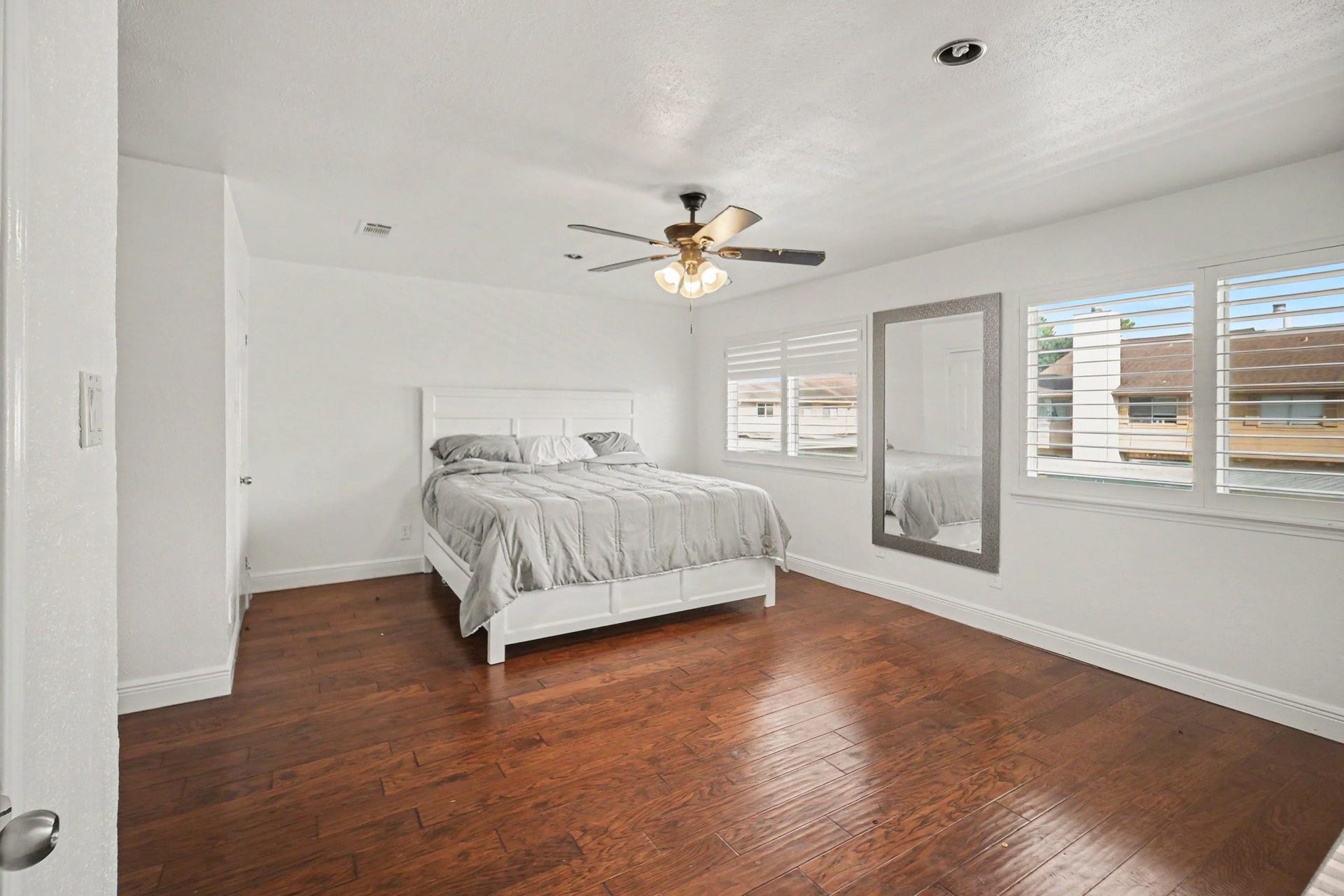 Spacious and bright, the primary bedroom offers elegant hardwood floors, a ceiling fan for comfort, and abundant natural light streaming through large windows with plantation shutters.