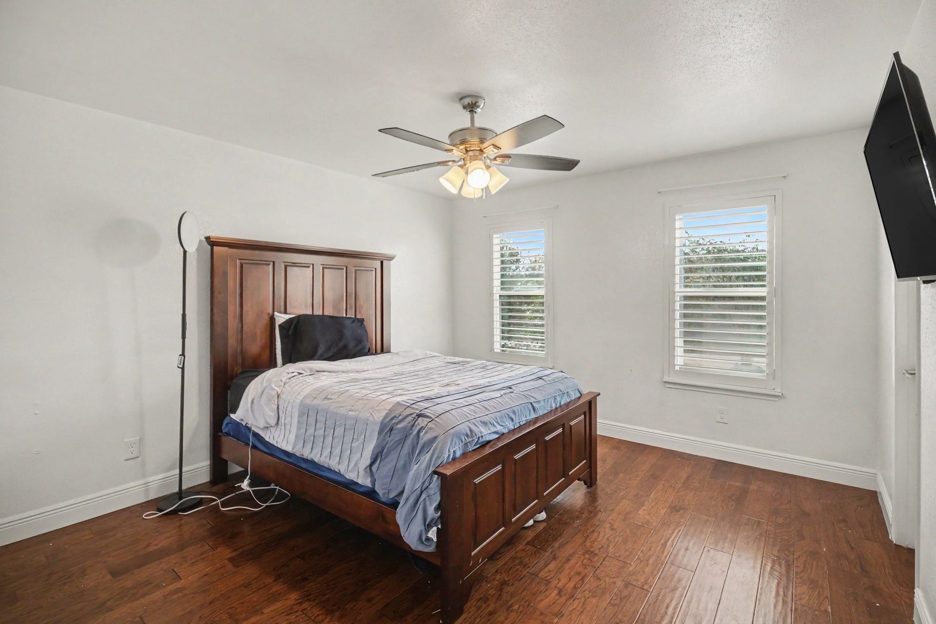 The second bedroom offers a cozy retreat with rich hardwood floors, ample natural light from dual windows, and a stylish ceiling fan for comfort and elegance.