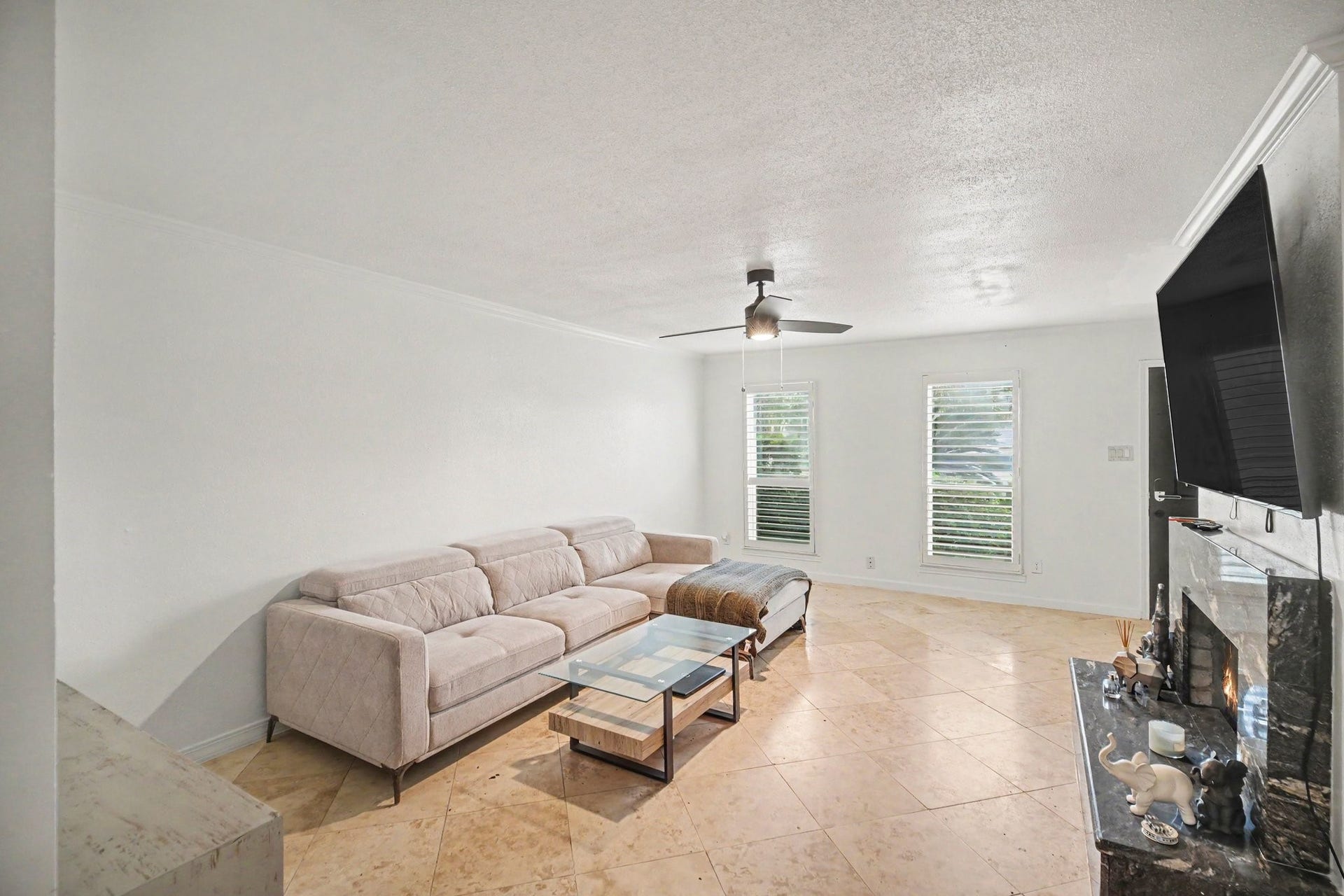 Spacious living room with a modern aesthetic, featuring a comfortable sectional sofa, sleek ceiling fan, and a cozy fireplace, complemented by natural light streaming through large windows.