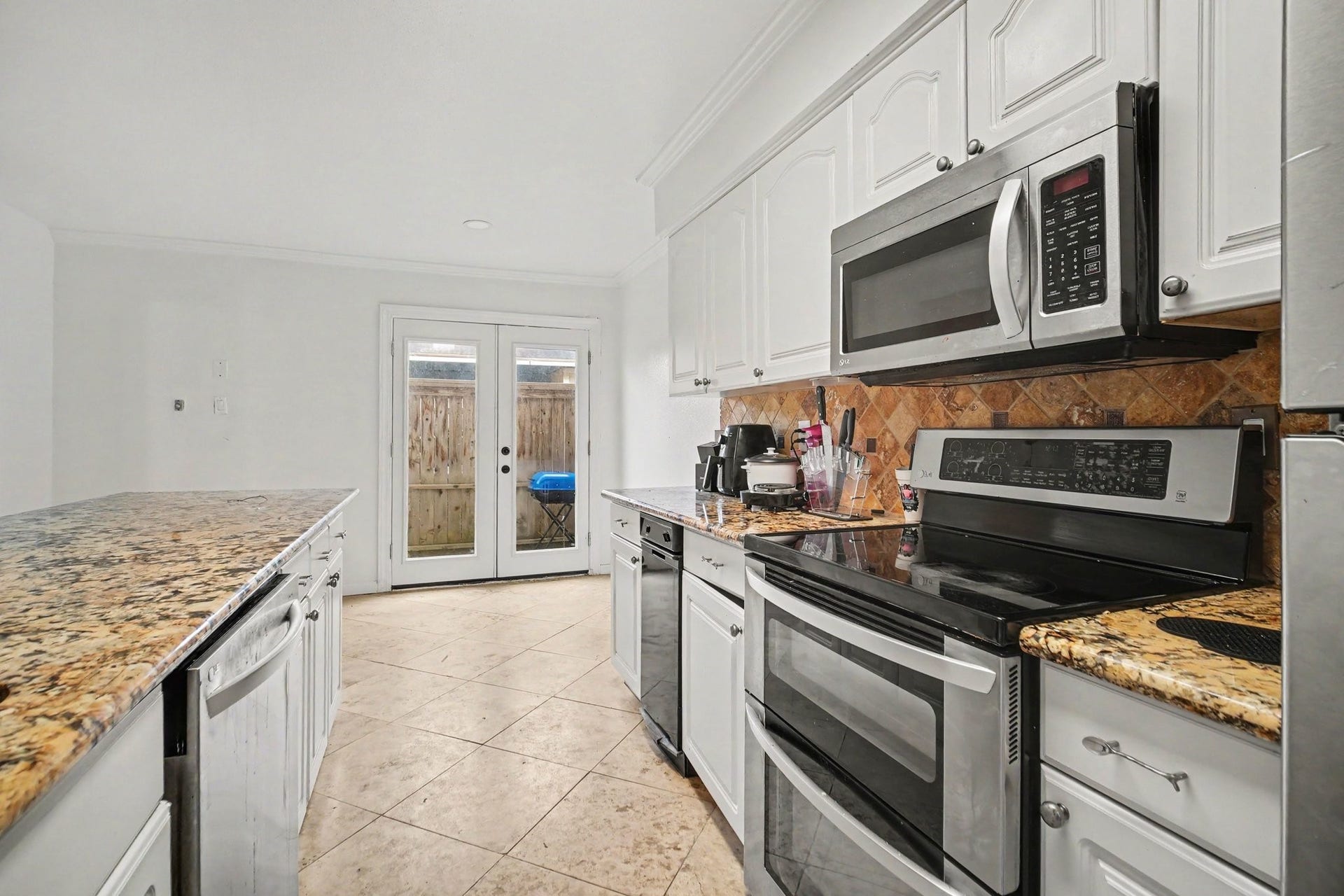 Bright and inviting kitchen with sleek stainless steel appliances, elegant granite countertops, and ample cabinetry, seamlessly opening to a charming outdoor space through French doors.