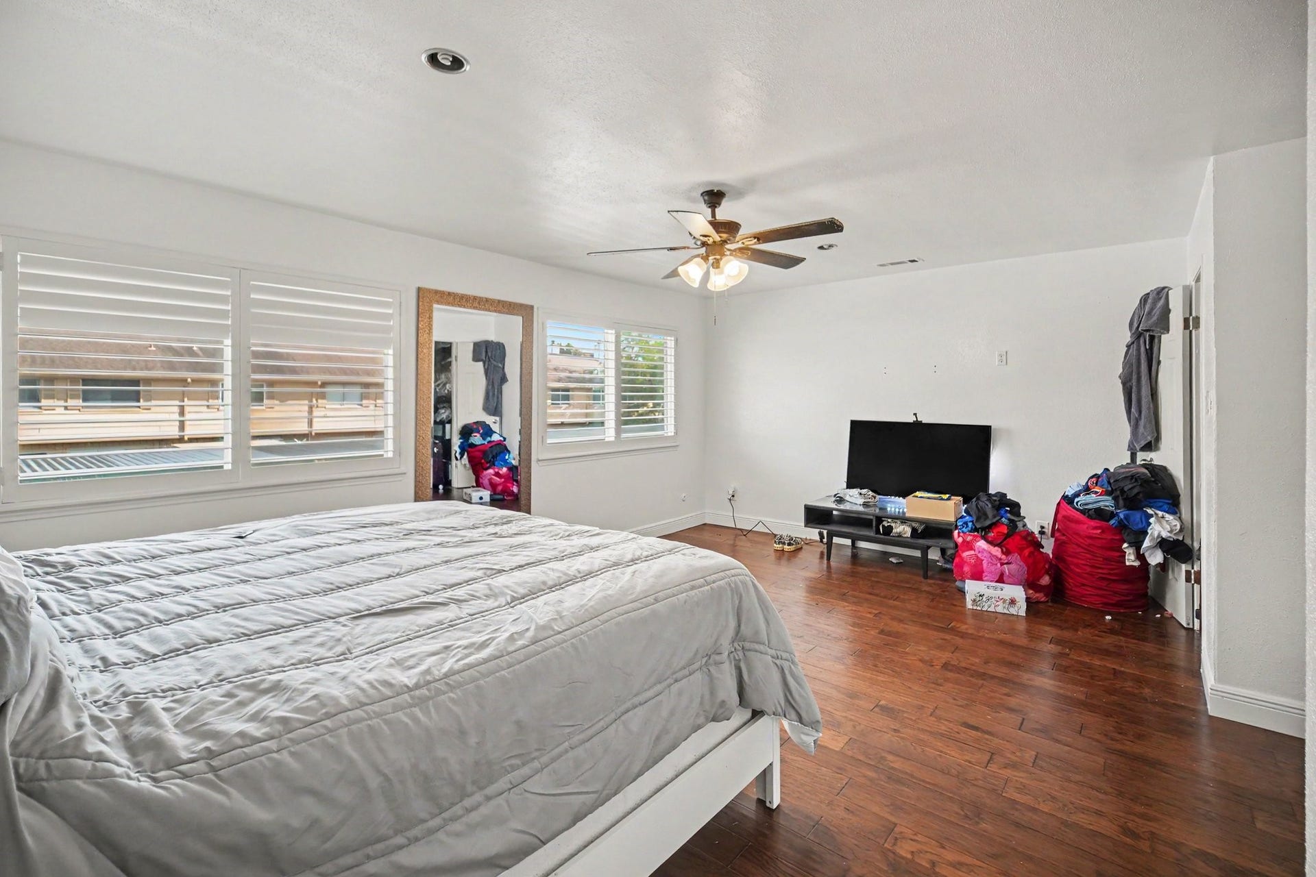 Spacious and inviting, the primary bedroom features rich hardwood floors, abundant natural light from large windows, and a ceiling fan for added comfort.
