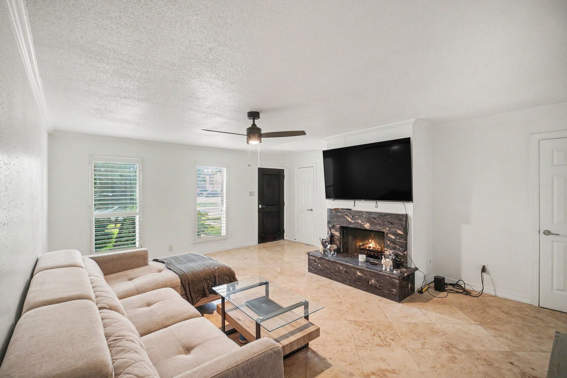 Experience modern comfort in this inviting living area, featuring a cozy fireplace, sleek tile flooring, and abundant natural light through large windows.