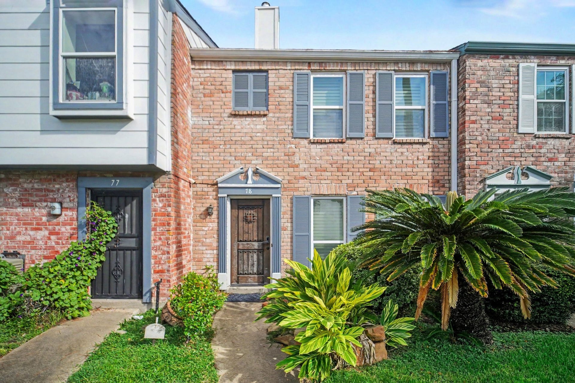 Charming brick townhouse with classic shutters and lush landscaping invites you through its welcoming front access.