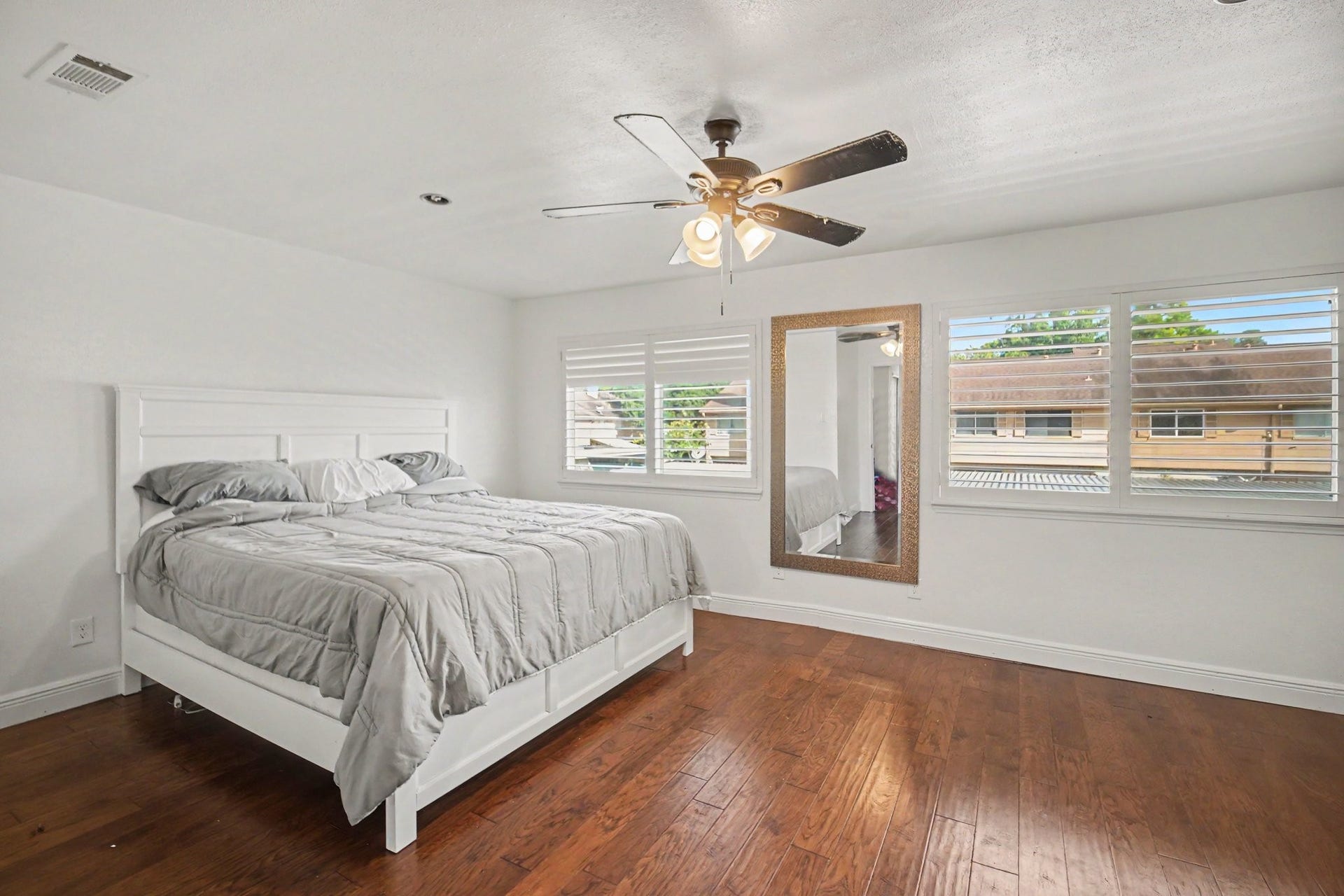 Experience comfort and style in this spacious primary bedroom, featuring elegant hardwood floors, abundant natural light through large windows, and a chic ceiling fan for the perfect retreat.