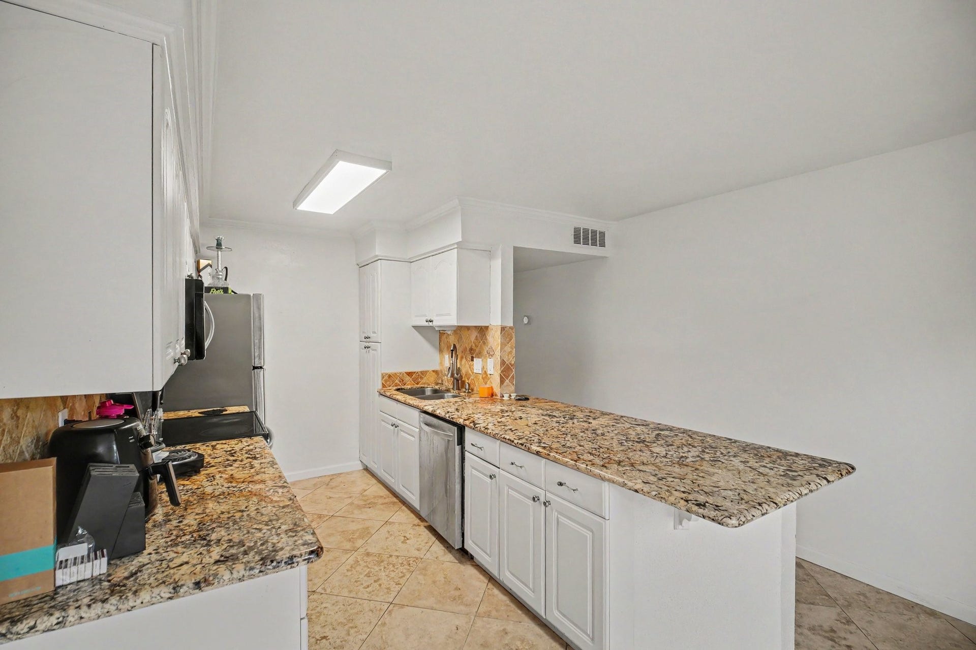 Experience culinary delight in this sleek kitchen featuring elegant granite countertops, pristine white cabinetry, and modern stainless steel appliances, all complemented by stylish tile flooring.
