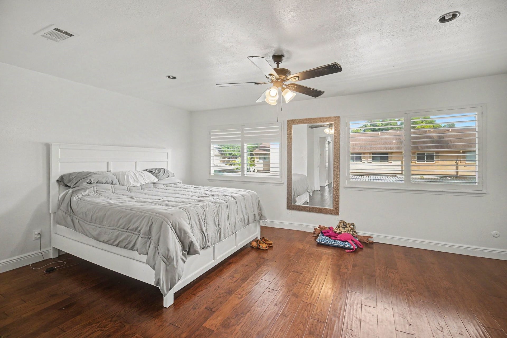 Discover the perfect retreat in this spacious primary bedroom, featuring elegant hardwood floors, abundant natural light from large windows, and a stylish ceiling fan for ultimate comfort.