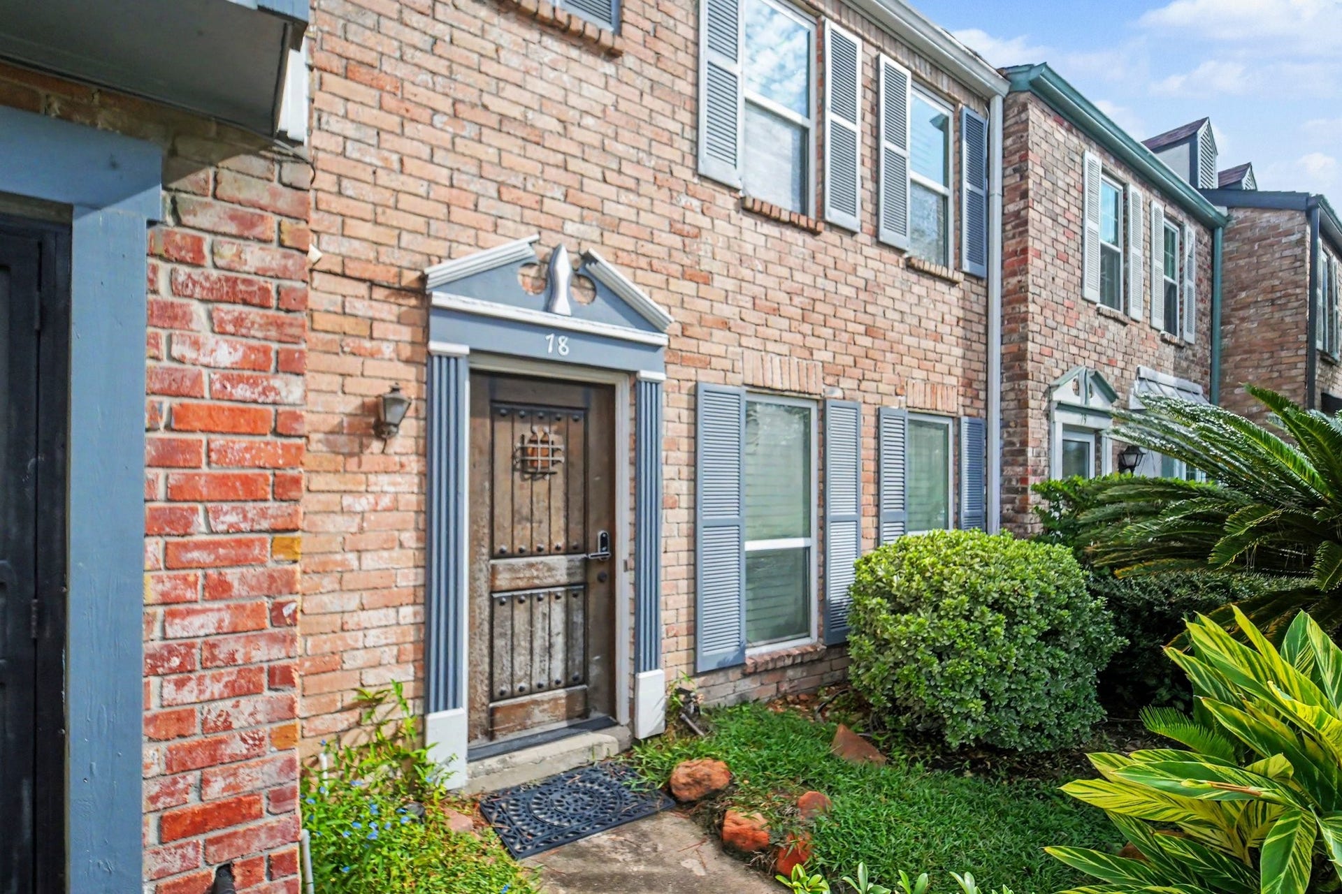 Charming brick facade with a welcoming front entry, framed by lush greenery and classic architectural details.