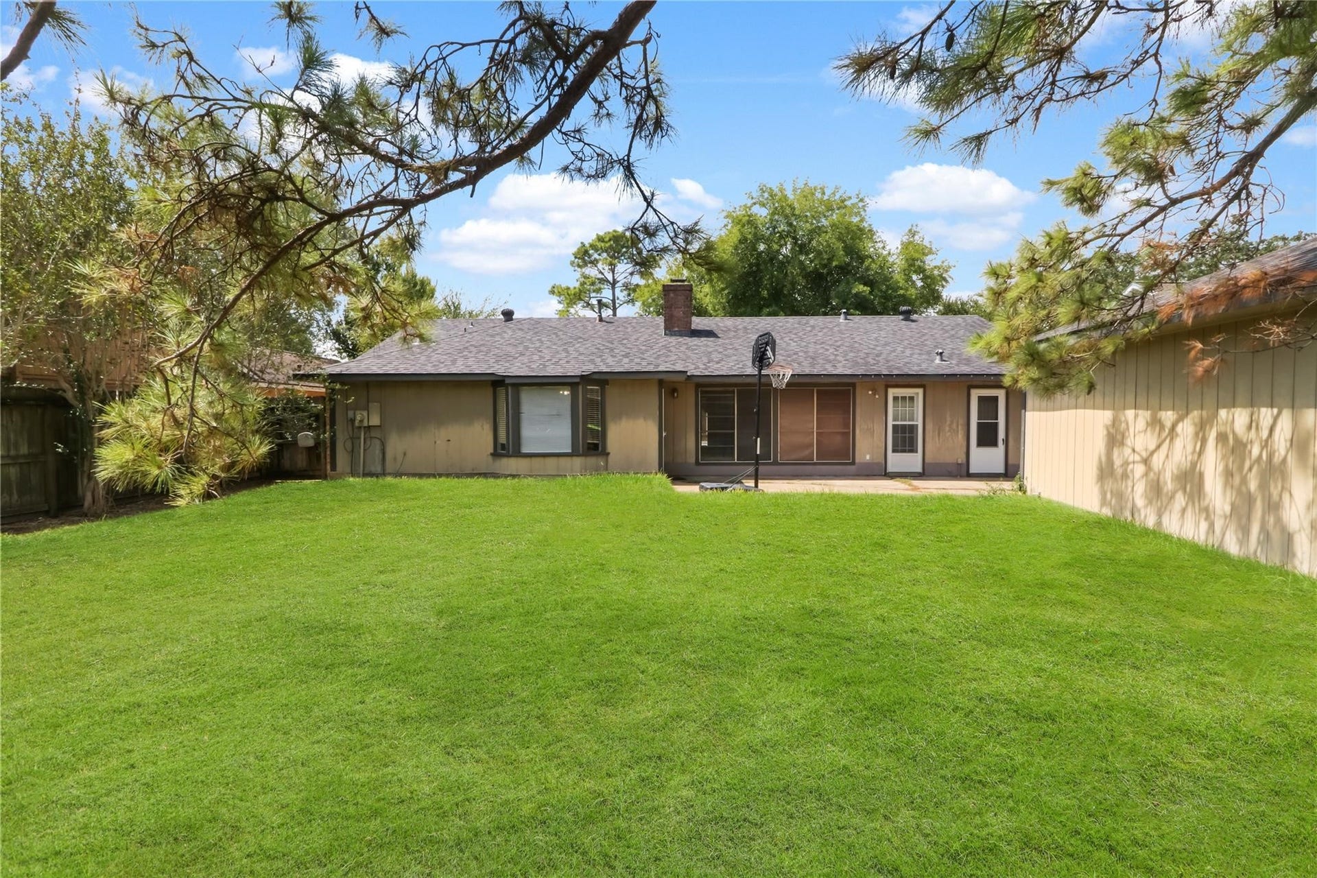 Spacious backyard with a large grassy area, mature trees, and plenty of room for outdoor activities and entertaining.