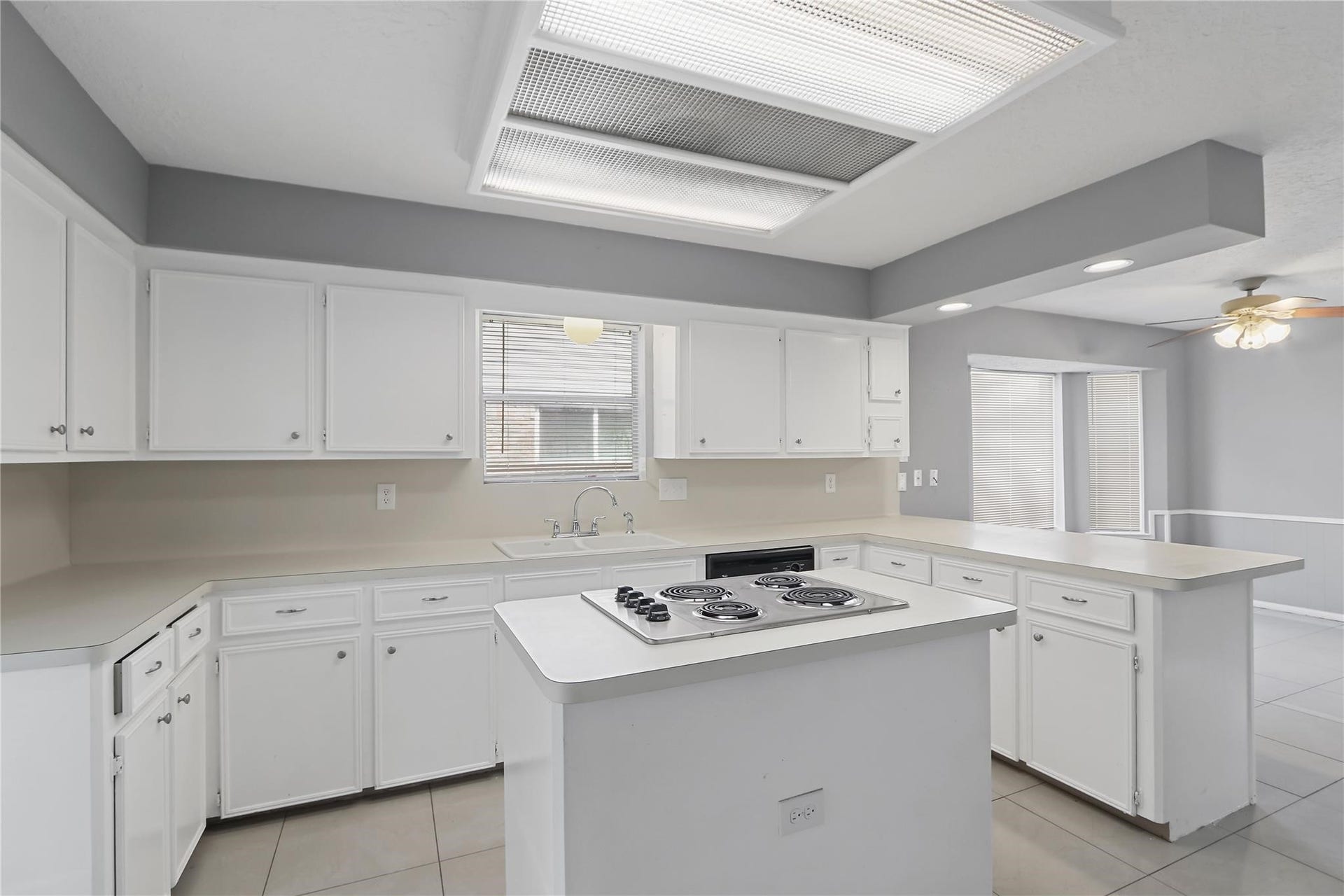 Another view of the kitchen, featuring generous cabinet and counter space, a center island with cooktop, and an open view into the breakfast area.