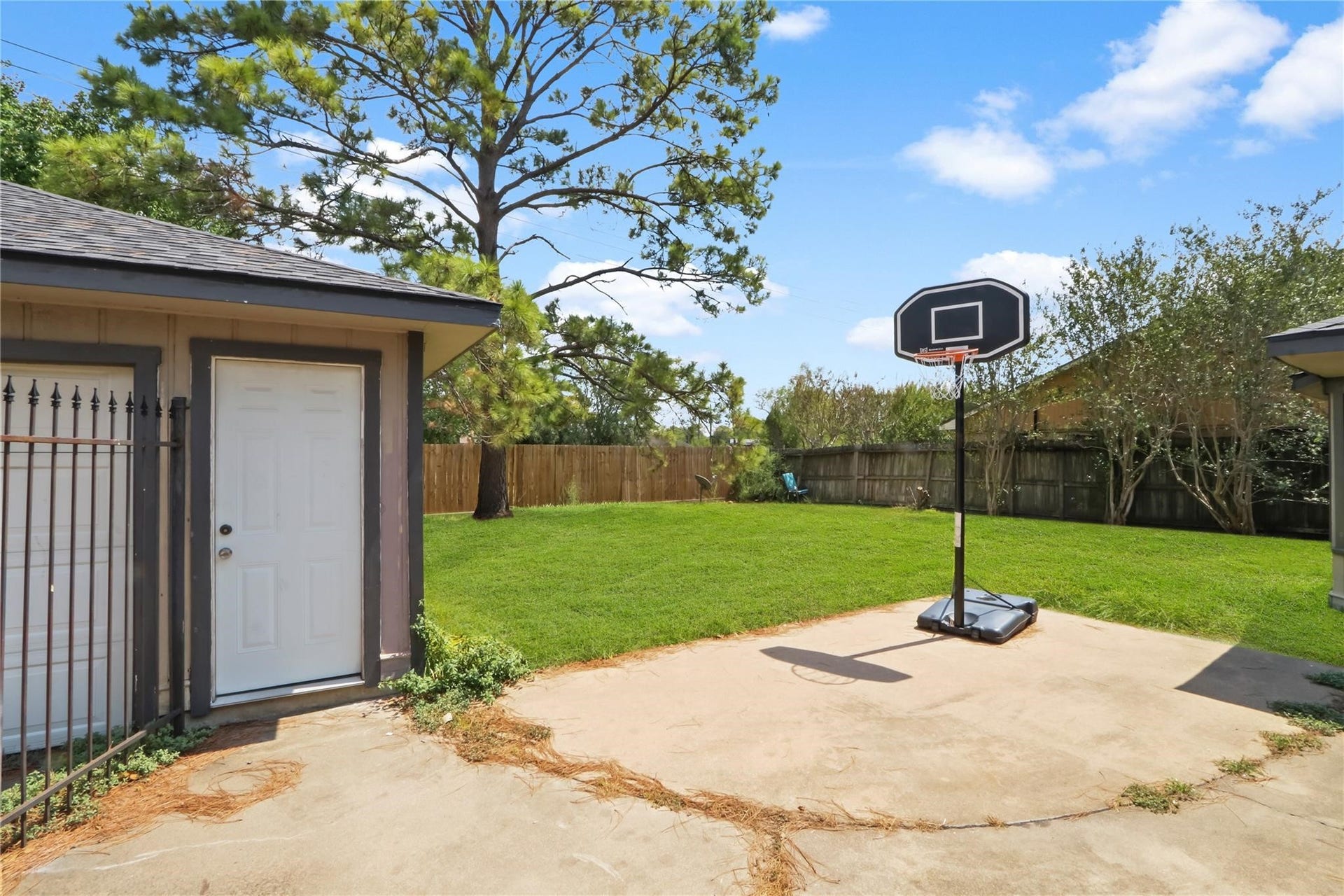 Another view of the spacious backyard, featuring a detached two-car garage, mature trees, and a concrete patio area with plenty of room for outdoor activities.