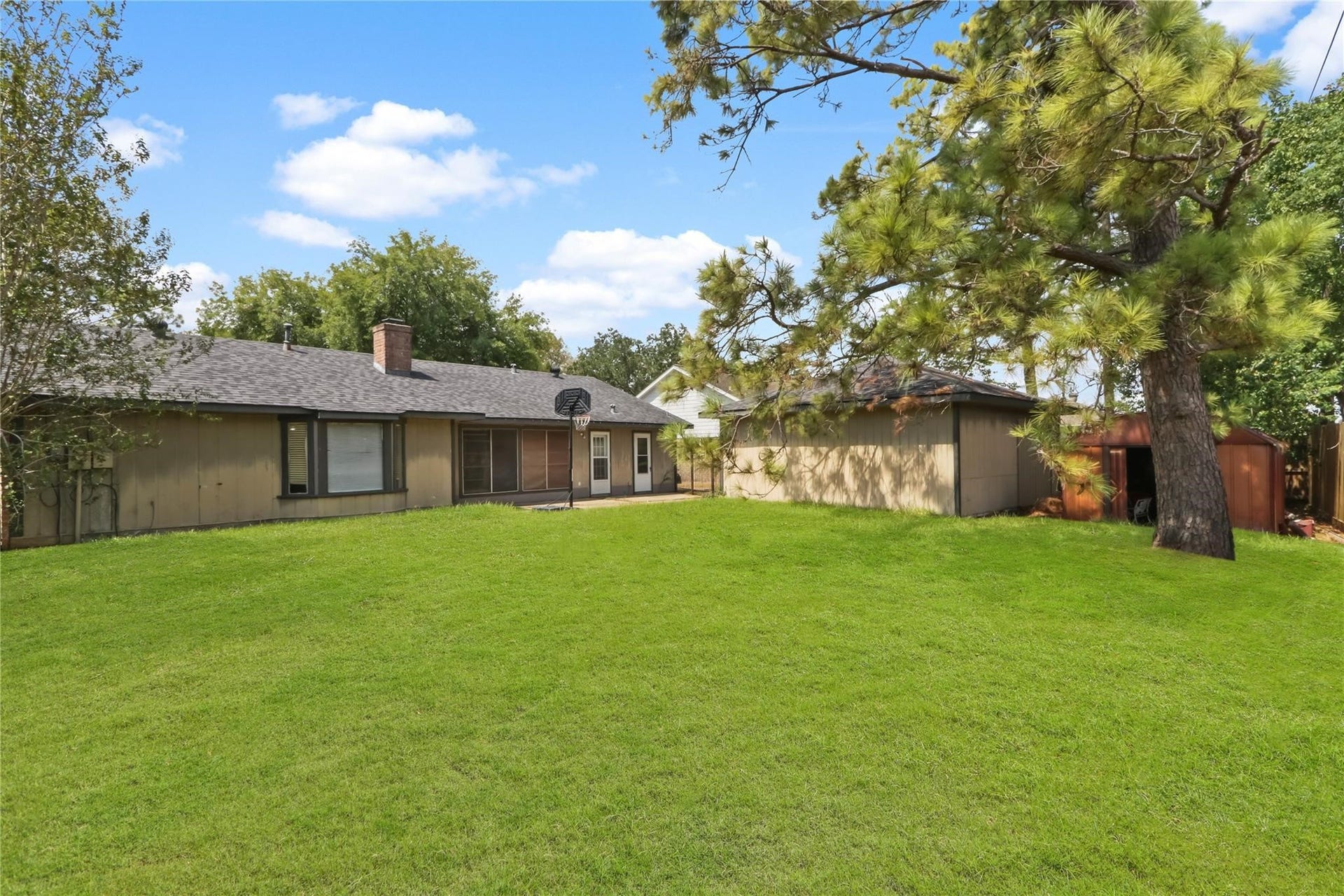 Spacious backyard with a large grassy area, mature shade trees, and a detached two-car garage.