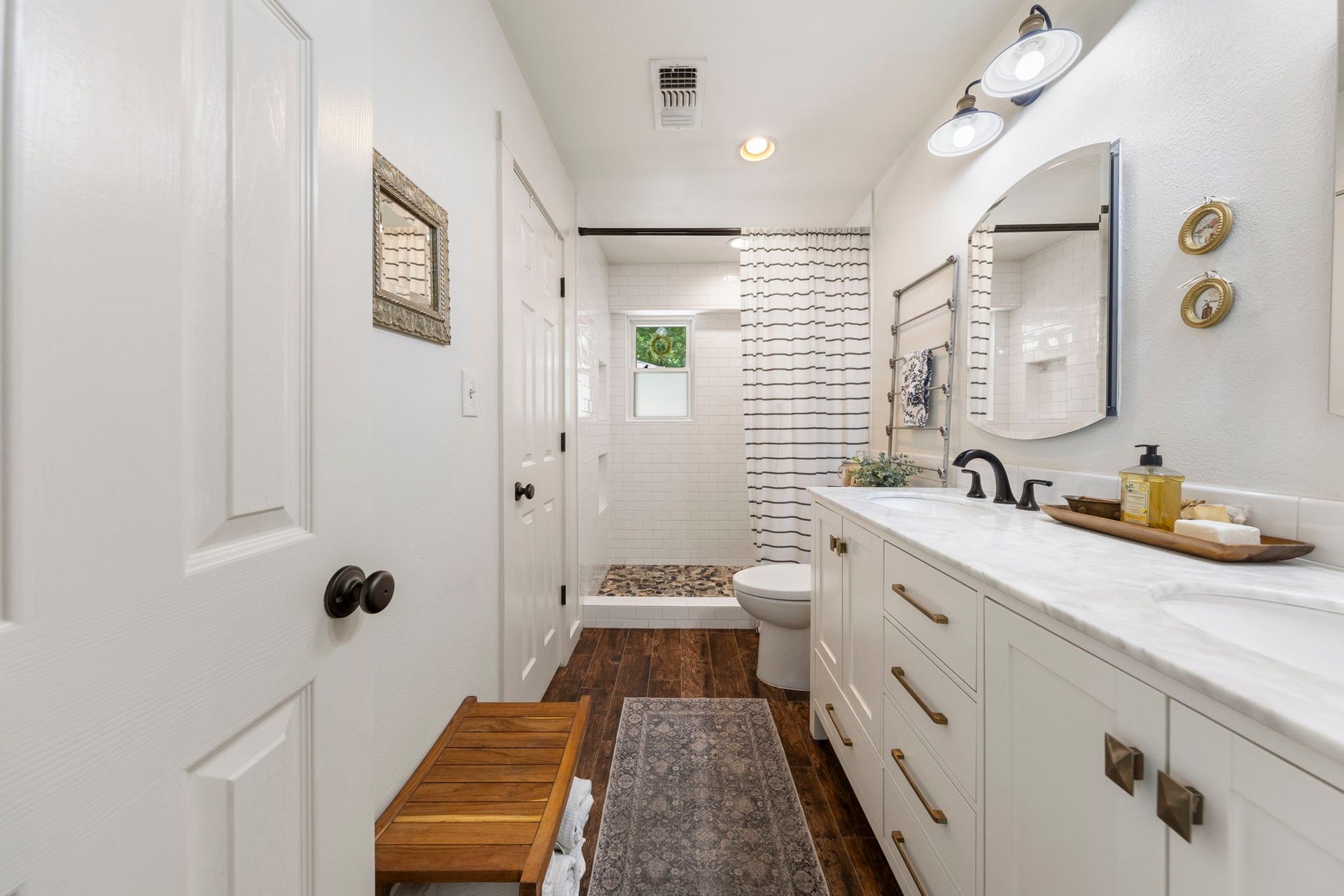 The beautifully renovated primary bath features a dual-sink vanity with quartz countertops, generous storage, and a walk-in shower with timeless subway tile and pebble stone flooring.