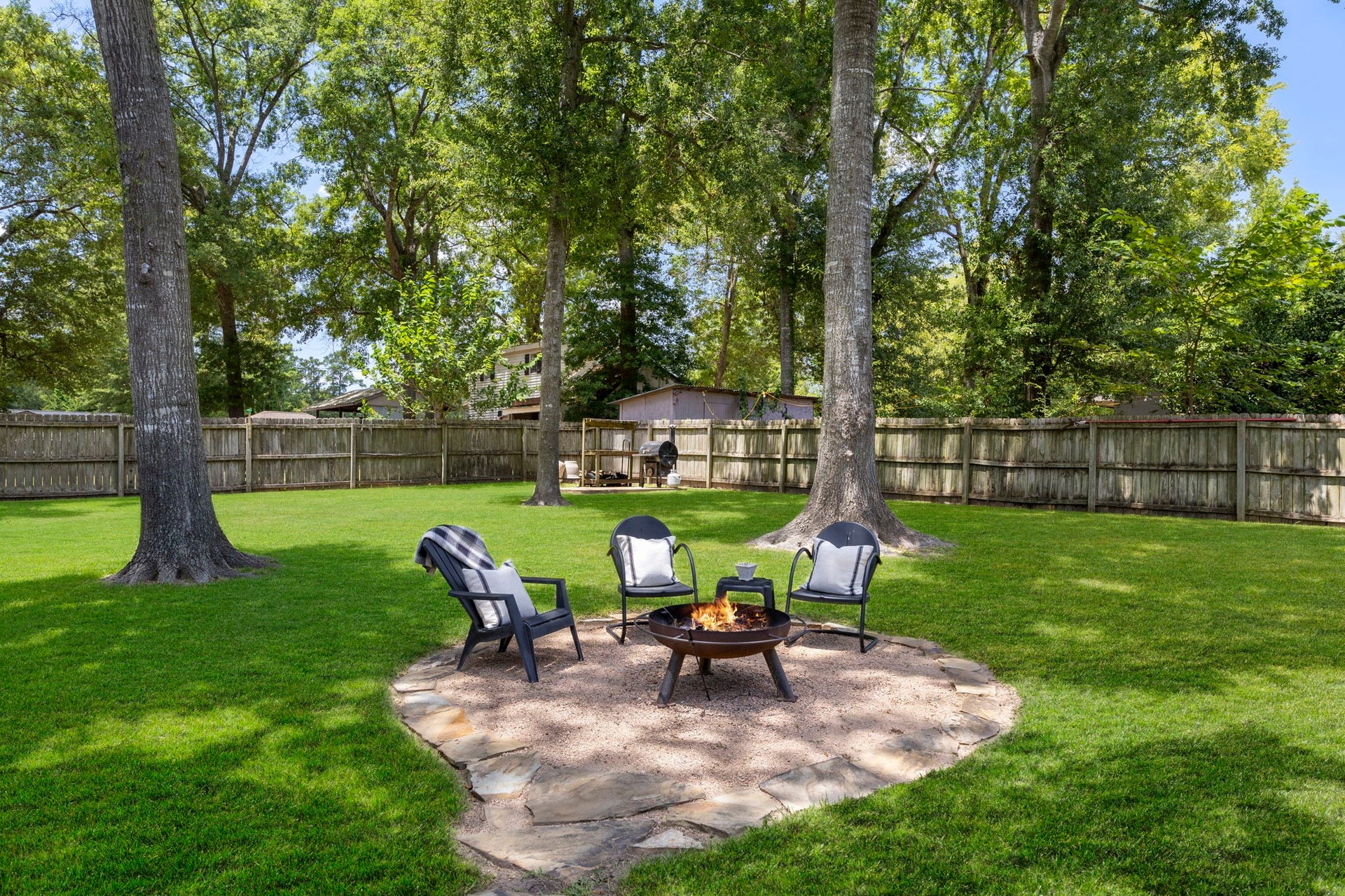 Expansive, private backyard with lush lawn, mature shade trees, and a charming fire pit gathering area.