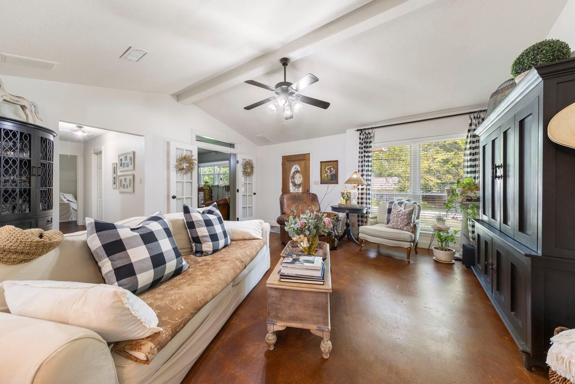 The inviting family room features vaulted ceilings with exposed beams, abundant natural light, and an open layout that flows seamlessly into the dining area and kitchen, creating an ideal space for everyday living and entertaining.