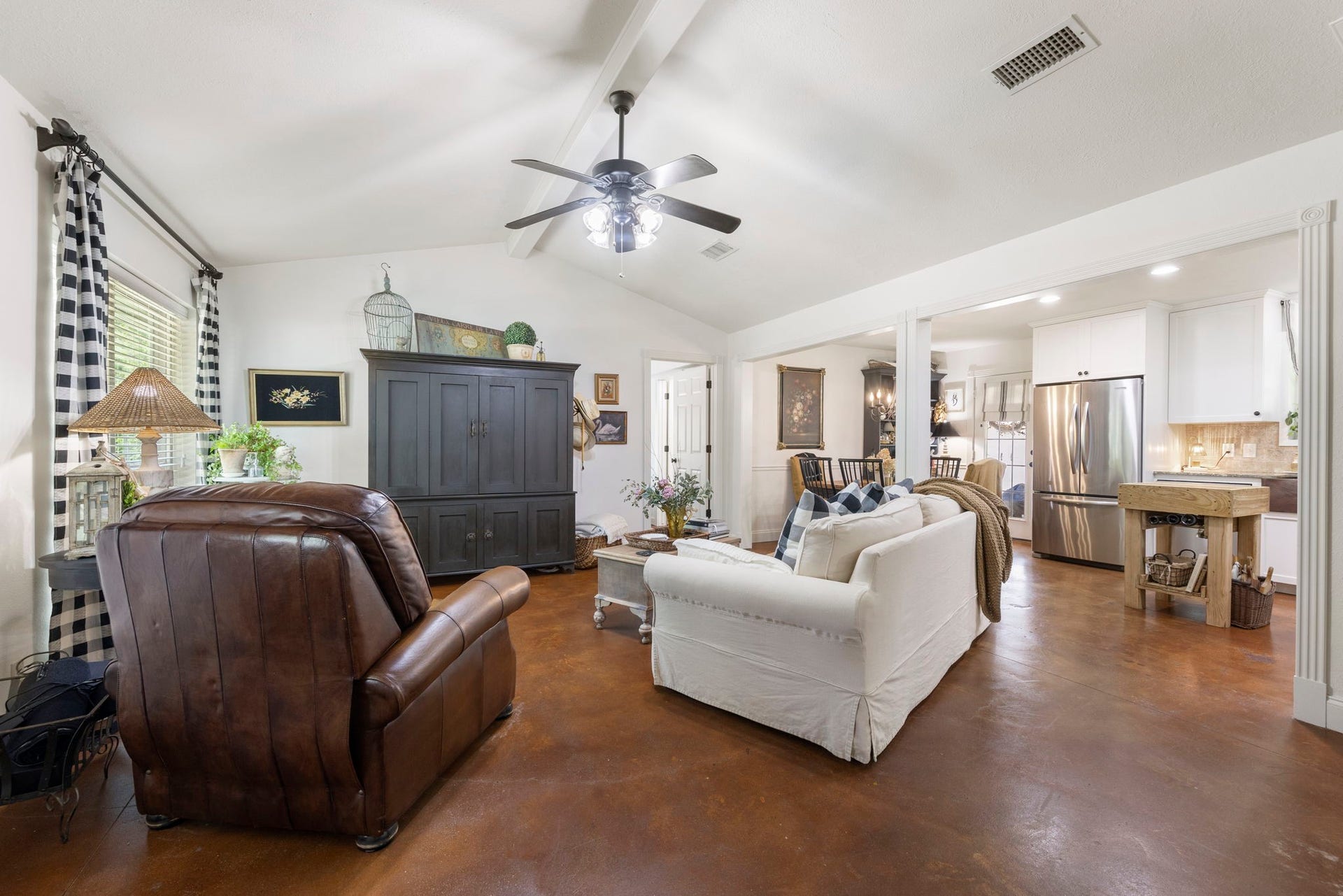 The spacious living room showcases soaring vaulted ceilings with exposed beams and an open-concept design, creating a warm, inviting atmosphere that flows effortlessly into the dining area and kitchenperfect for everyday living and entertaining.