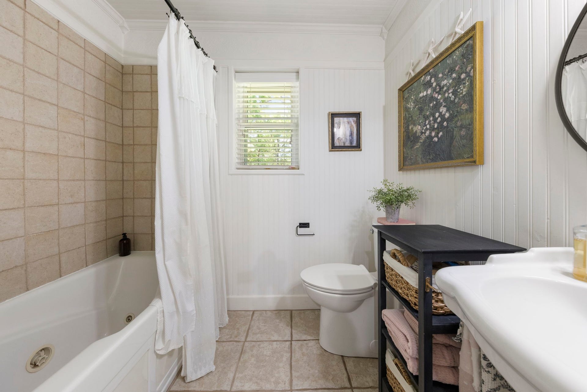 The secondary bathroom features a tub/shower combination, beadboard accent walls, natural light, and convenient open shelving for additional storage and everyday essentials.