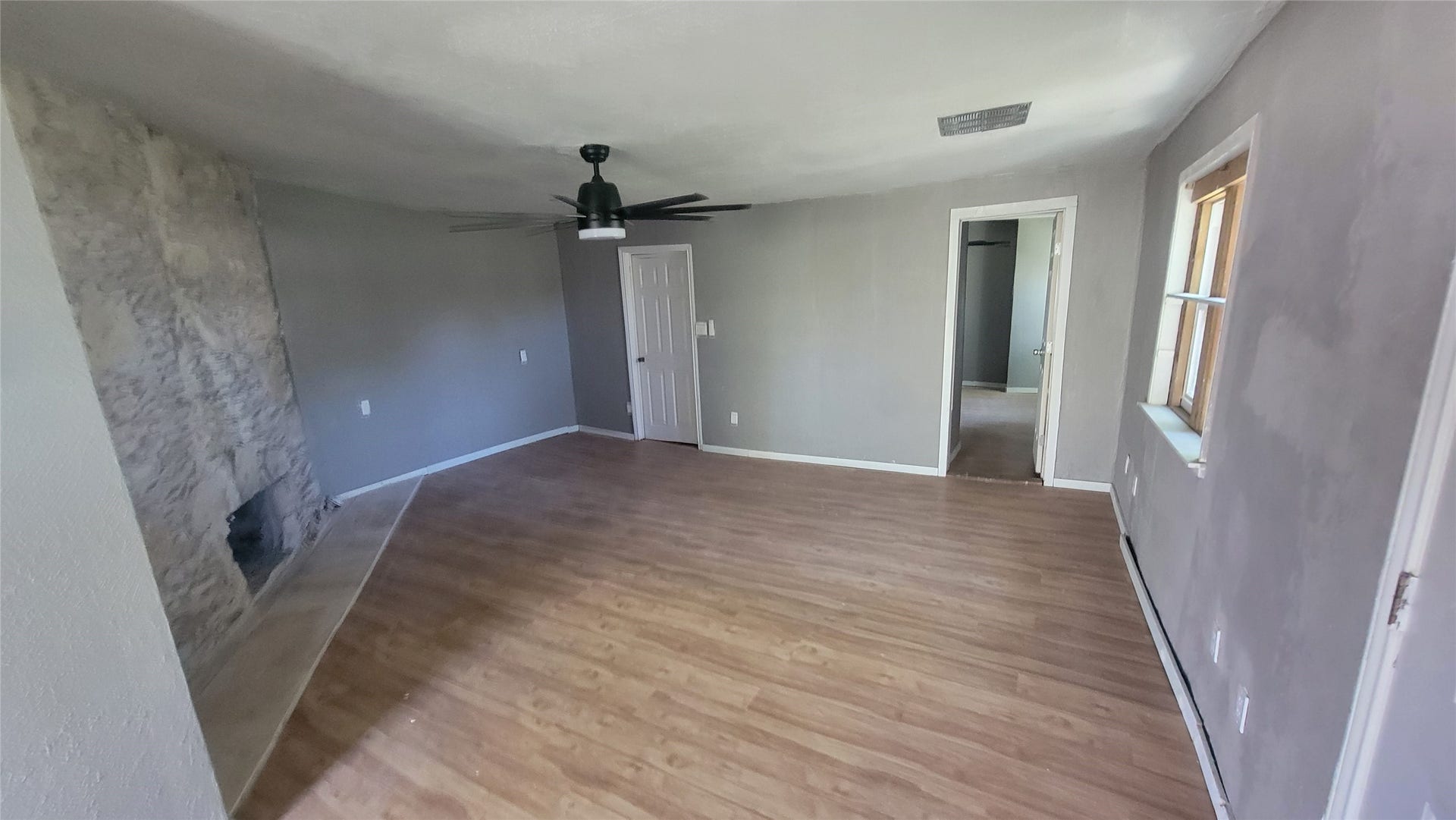 12018 Sandpiper Road, Angleton, TX 77515 This room features a clean, modern look with light wood flooring and neutral gray walls. It includes a stone fireplace for a cozy touch, a ceiling fan for comfort, and ample natural light from a window. There is also a doorway leading to an adjacent space, offering versatile use potential.