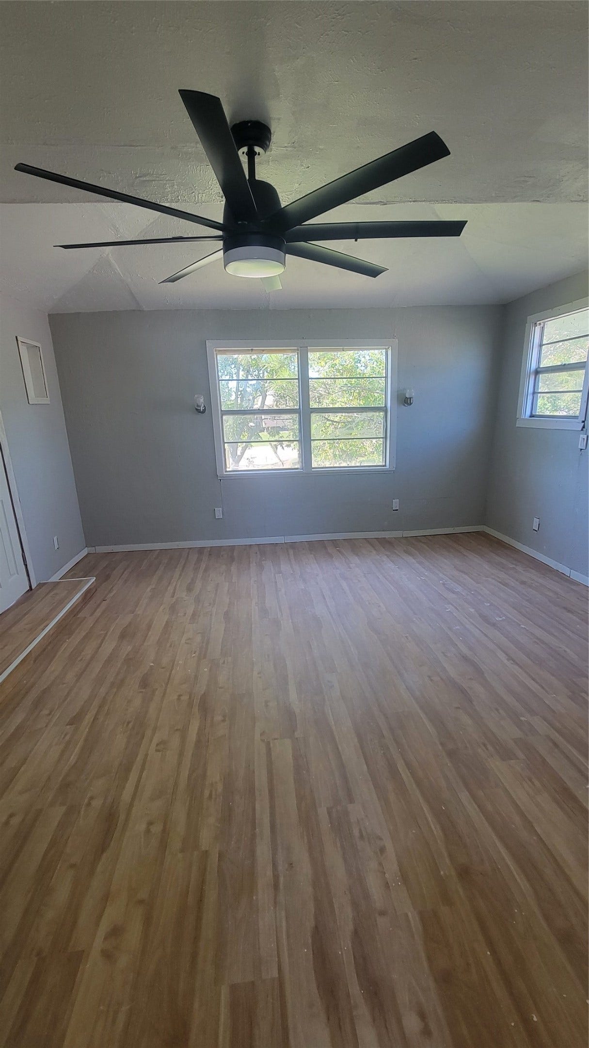 12018 Sandpiper Road, Angleton, TX 77515 This room features light wood flooring, neutral gray walls, large windows for natural light, and a modern ceiling fan, creating a bright and airy space.