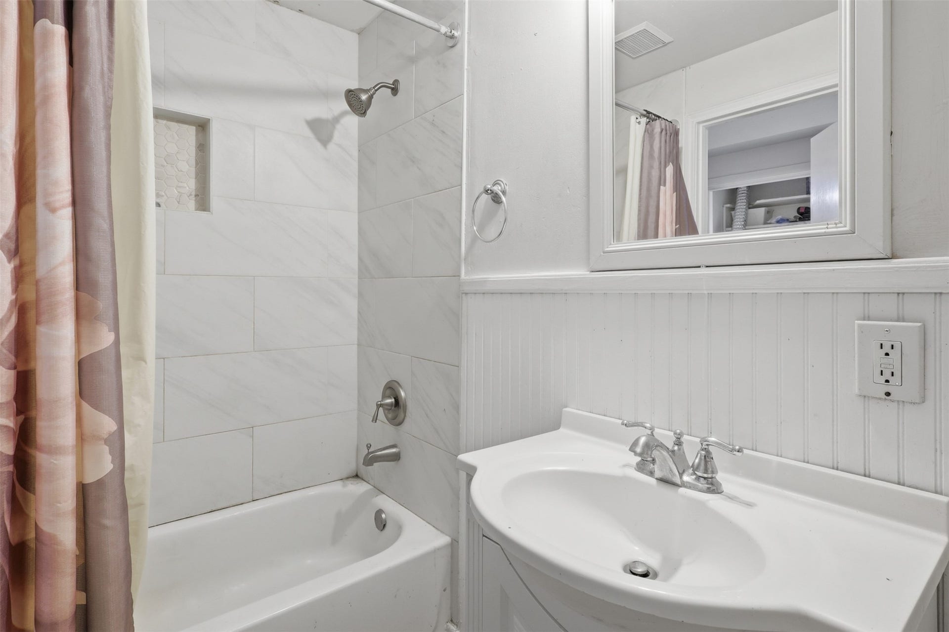 Tastefully updated shower area featuring modern large-format tile surround, recessed storage niche, and classic beadboard accents.