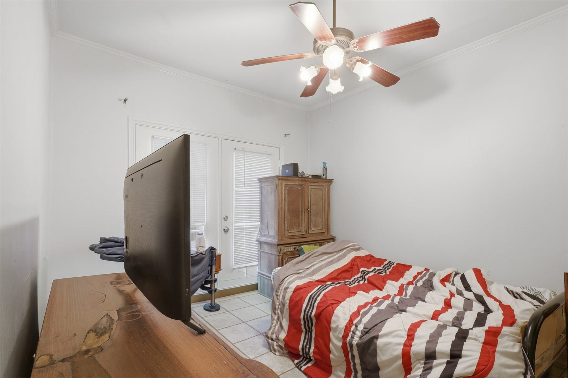 Sunlit secondary bedroom enjoying classic French doors that open directly outside, paired with durable tiled floors.