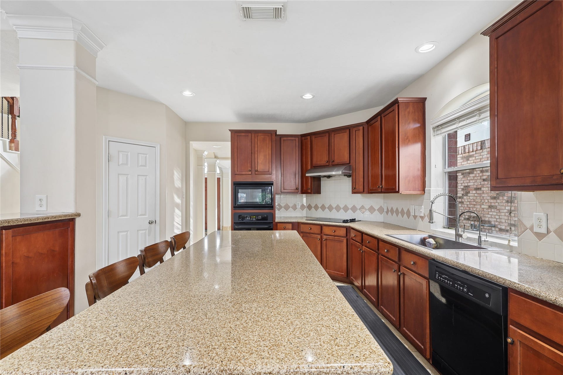 2614 Sunset Lake Drive, Sugar Land, TX 77478 This spacious kitchen features elegant wood cabinetry, a large granite island with seating, and modern appliances, offering a bright and functional space for cooking and entertaining.