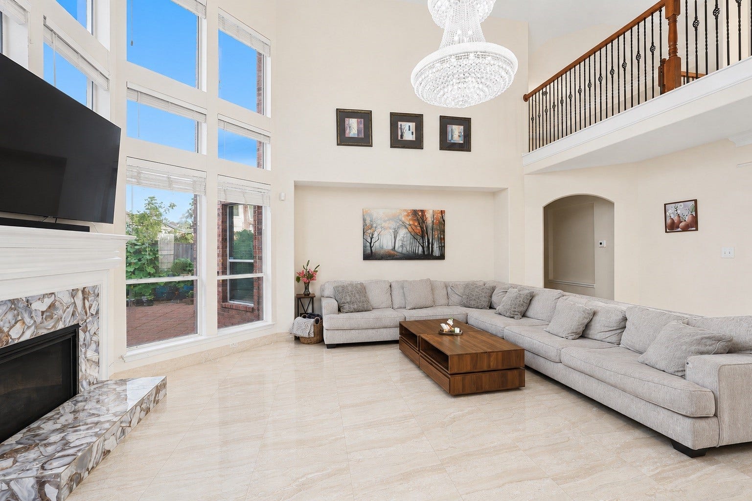 2614 Sunset Lake Drive, Sugar Land, TX 77478 This spacious living room features high ceilings, large windows for natural light, a modern chandelier, and a cozy sectional sofa. It includes a stylish fireplace, elegant tile flooring, and a wooden coffee table, creating a welcoming and luxurious atmosphere.